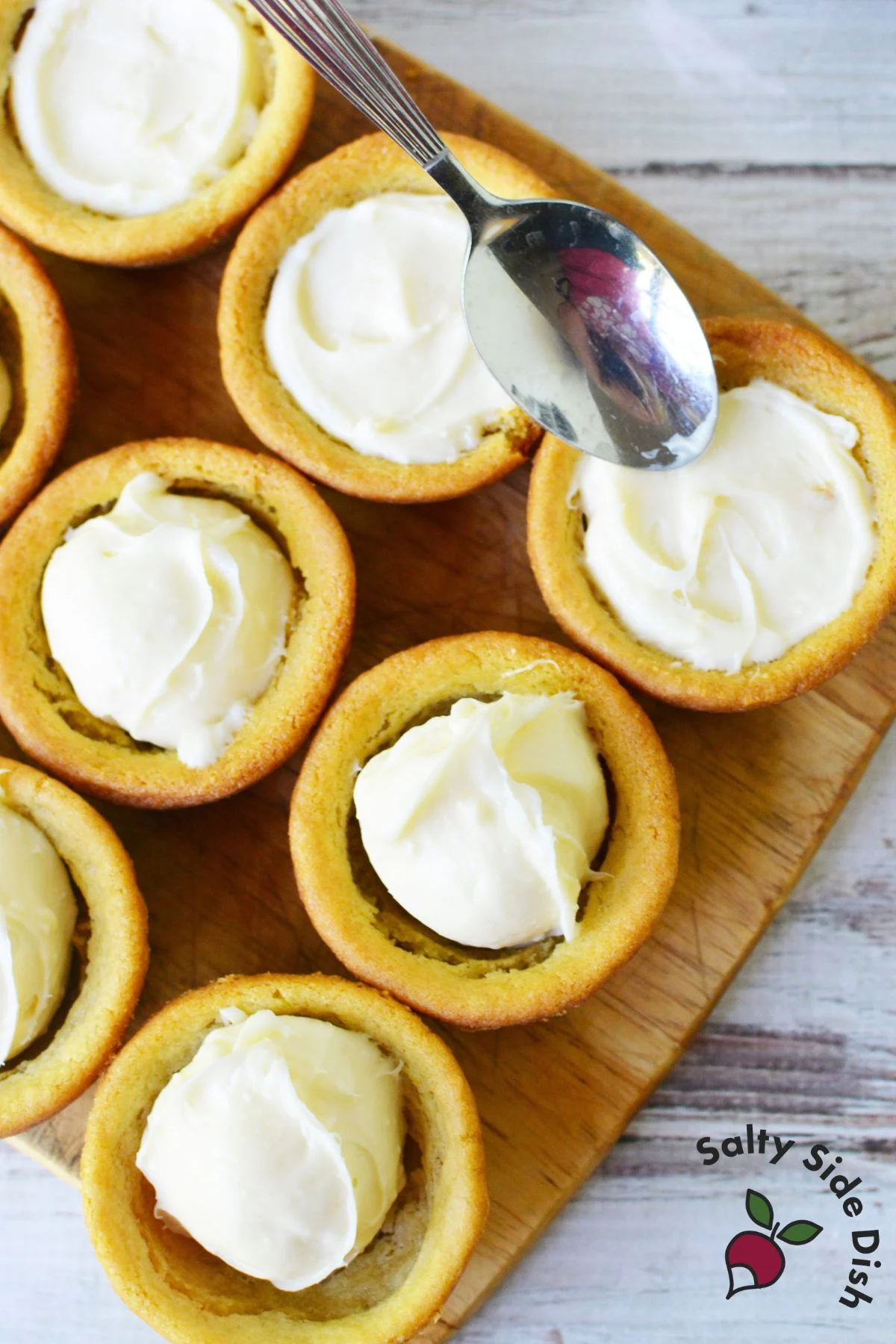Spreading cream cheese filling into baked sugar cookie cups with a spoon