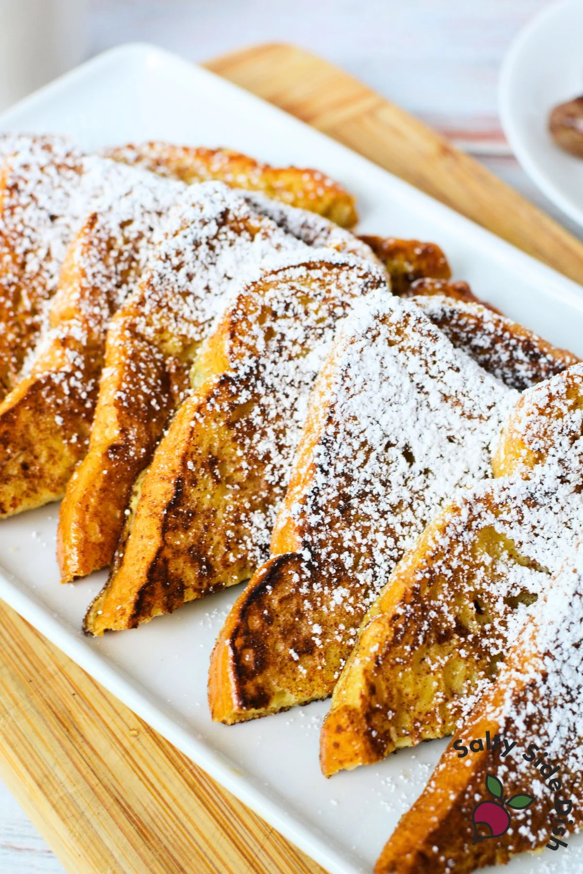 Close-up of brioche French toast slices topped with powdered sugar and syrup for a sweet, custardy breakfast.
