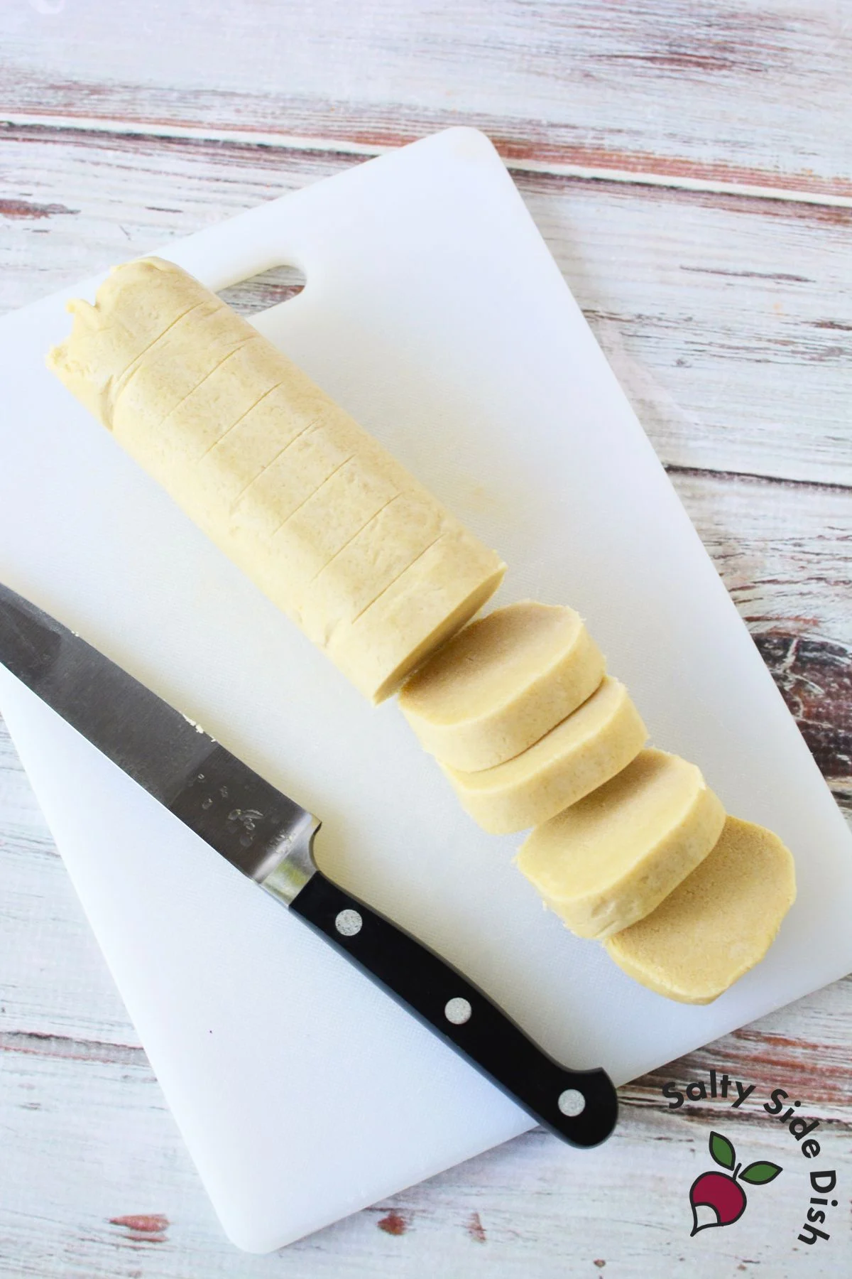 Slicing refrigerated sugar cookie dough log into even rounds on a cutting board