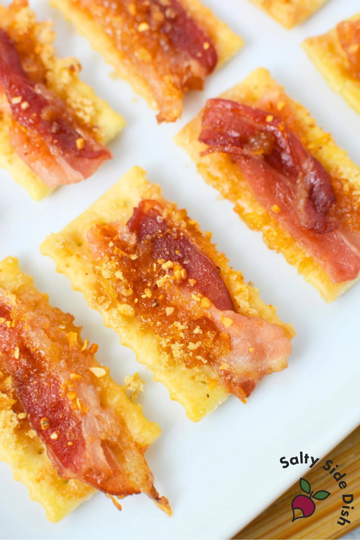 Close-up of finished candied bacon crackers with golden brown bacon on club crackers, served on white platter
