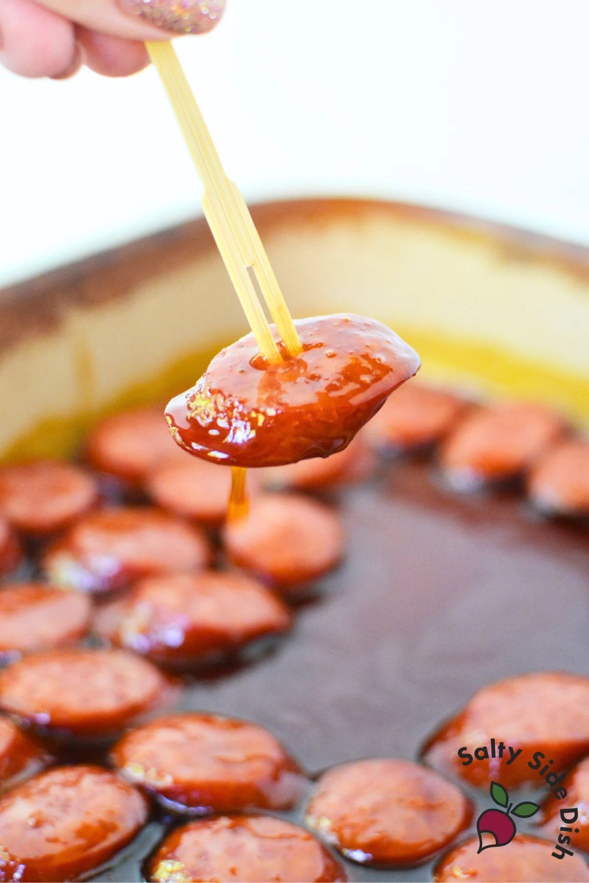 Single sausage slice dipped in BBQ glaze lifted on appetizer toothpick for serving