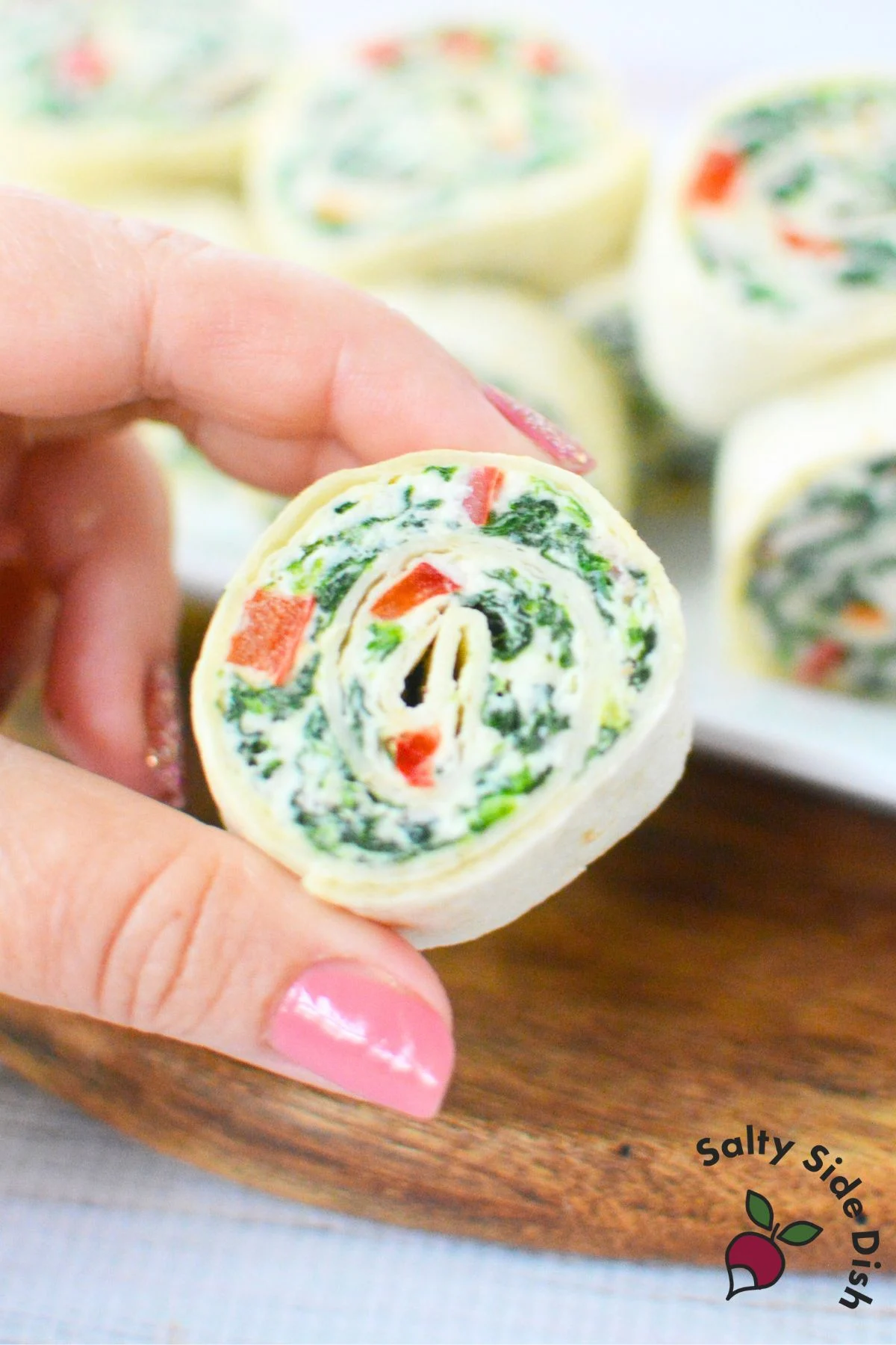 Close-up of hand holding a sliced spinach pinwheel appetizer with visible red pepper and spinach layers
