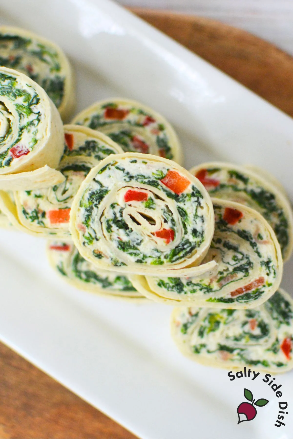 Sliced spinach dip tortilla roll ups arranged on a white serving platter