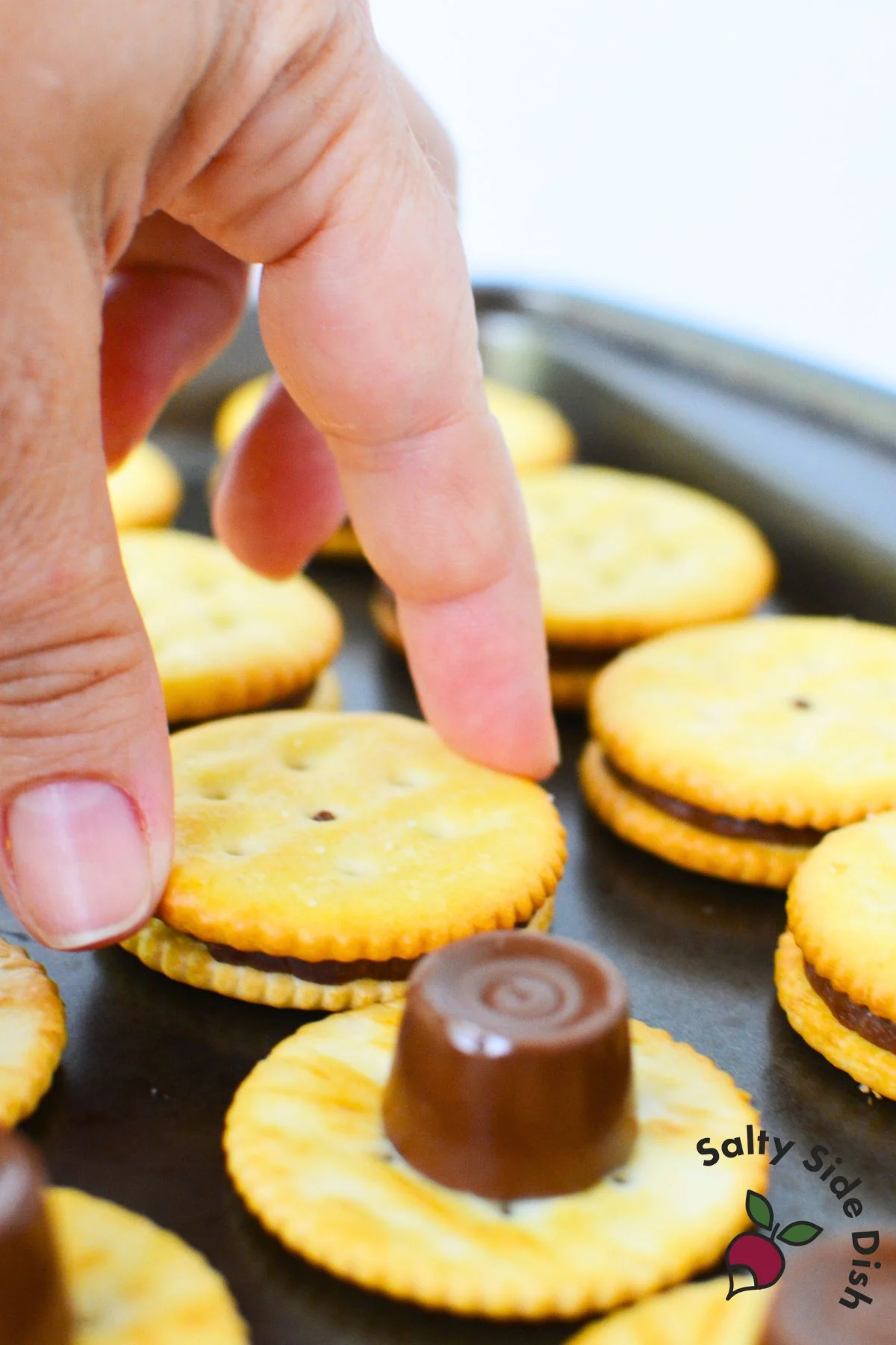 Hand pressing second Ritz cracker over melted Rolo candy to make sandwich cookie