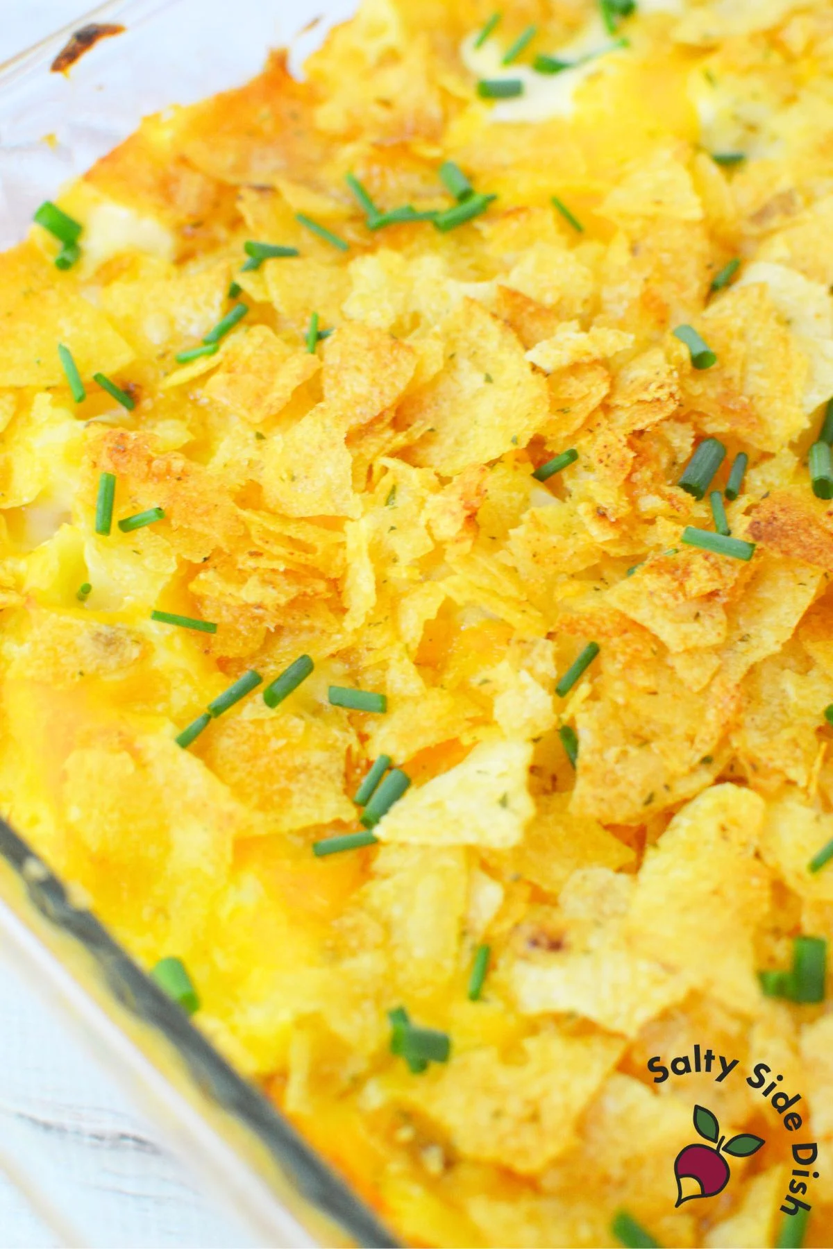 Baked potato casserole with crushed sour cream and onion chips and fresh chives on top for a crispy finish.