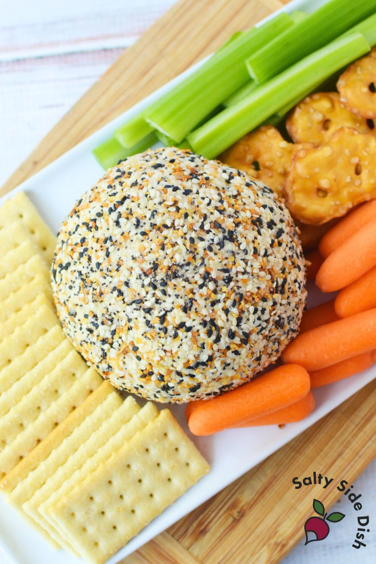 Everything bagel cheese ball served with carrots, celery, and crackers on a white plate