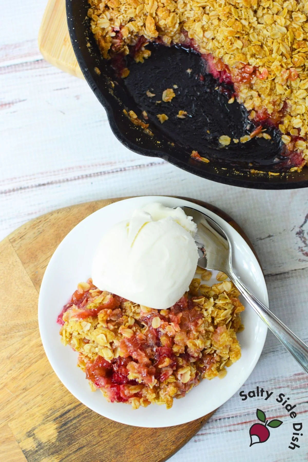Overhead view of a plate of rhubarb crisp with vanilla ice cream next to the cast iron skillet.