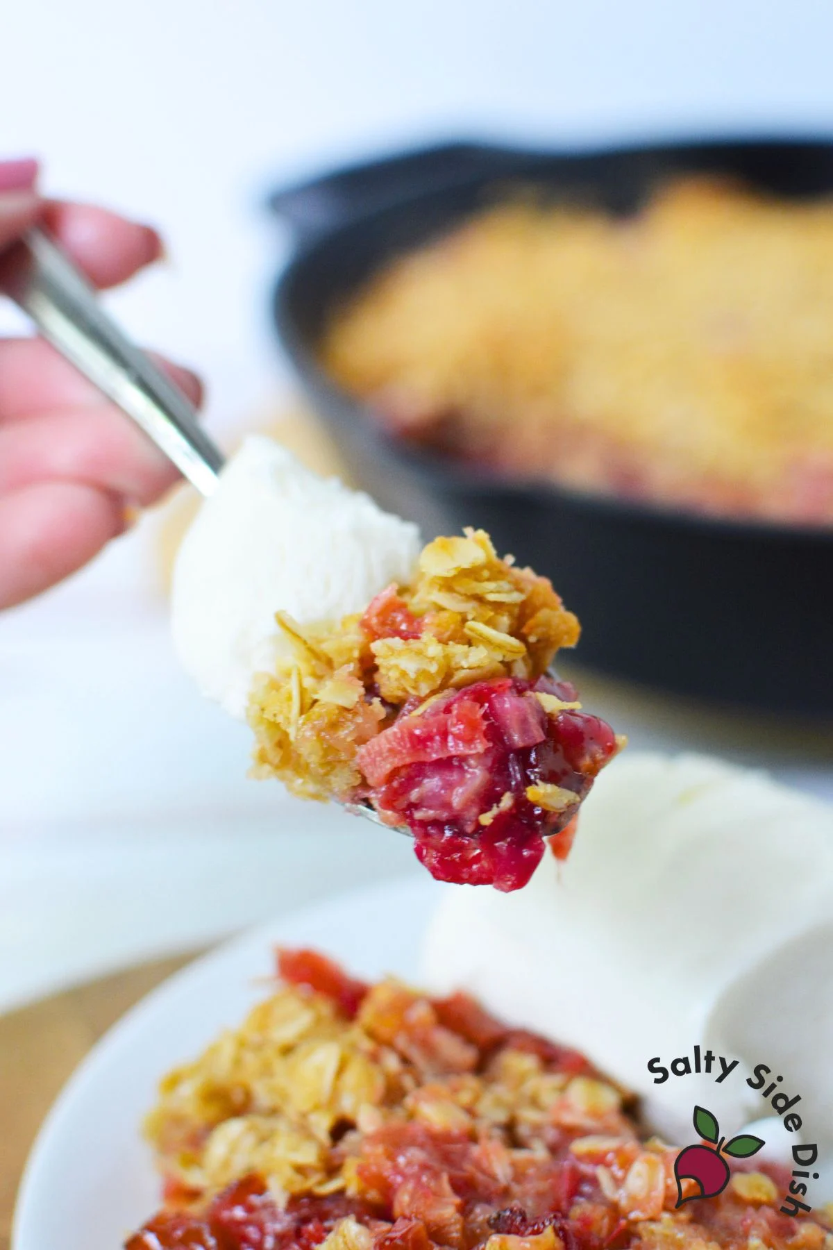Spoonful of warm rhubarb crisp with oats and vanilla ice cream.