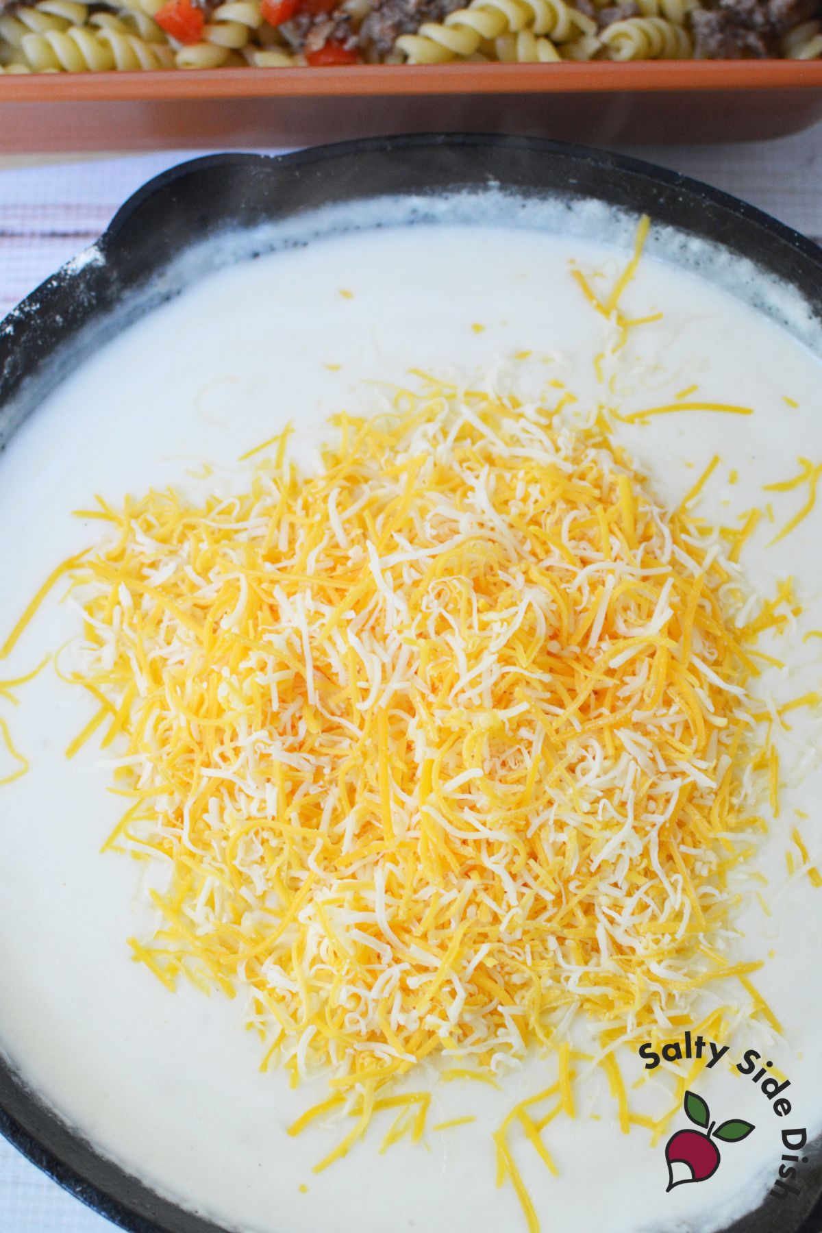 shredded colby jack cheese melting into a creamy white sauce for sausage pasta bake