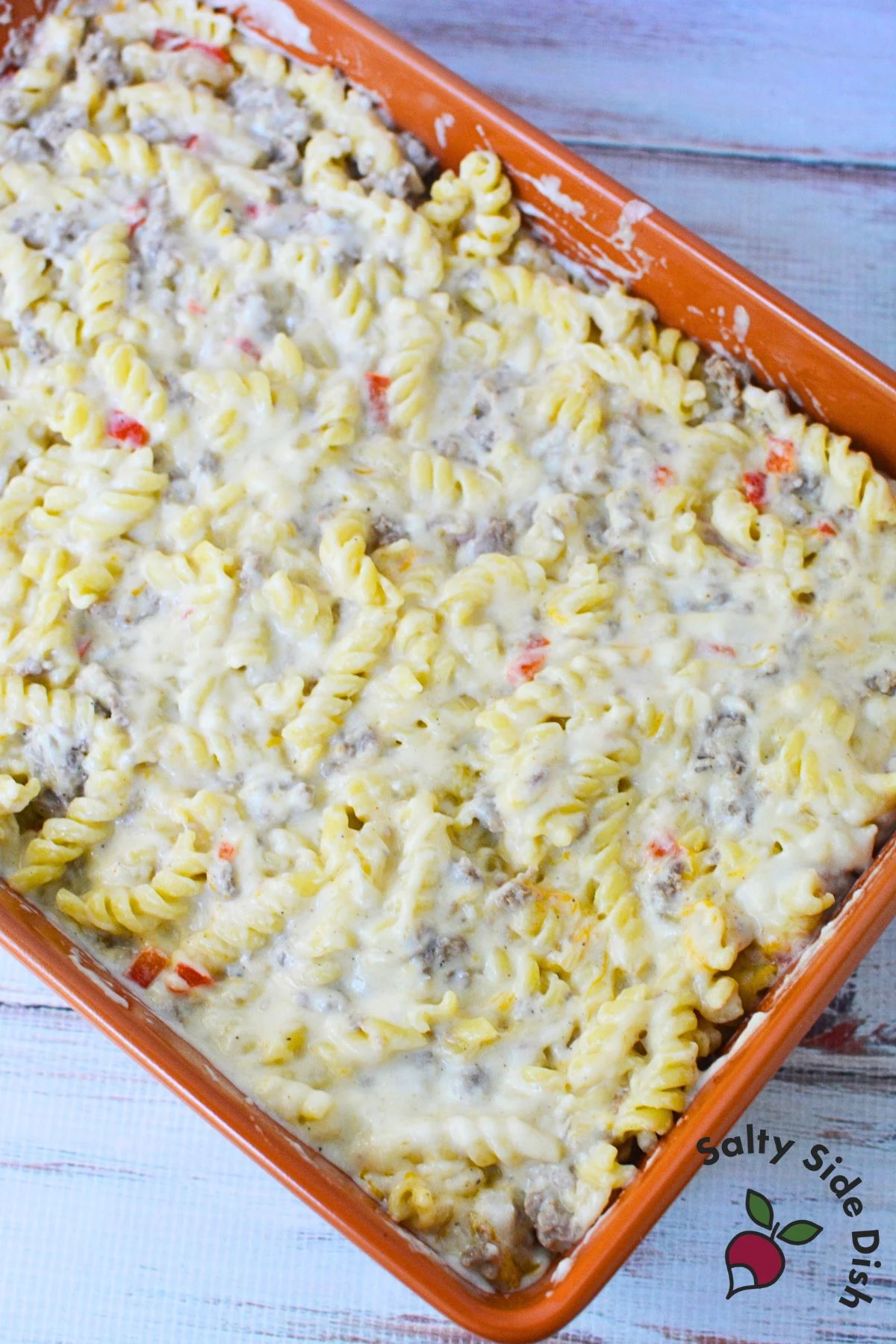 creamy cheese sauce coating rotini pasta, sausage, and peppers in a casserole pan