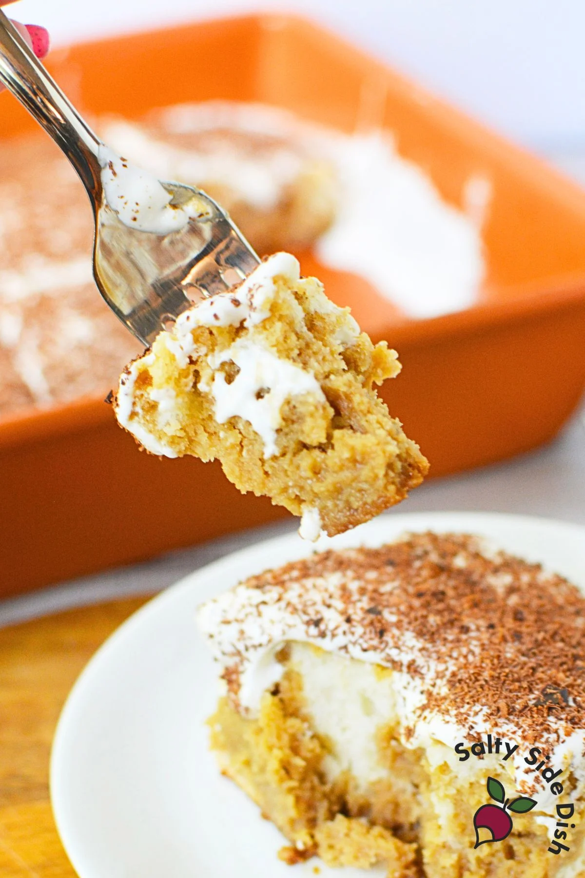 Fork holding a bite of coffee-soaked tiramisu poke cake with mascarpone cream and grated chocolate.