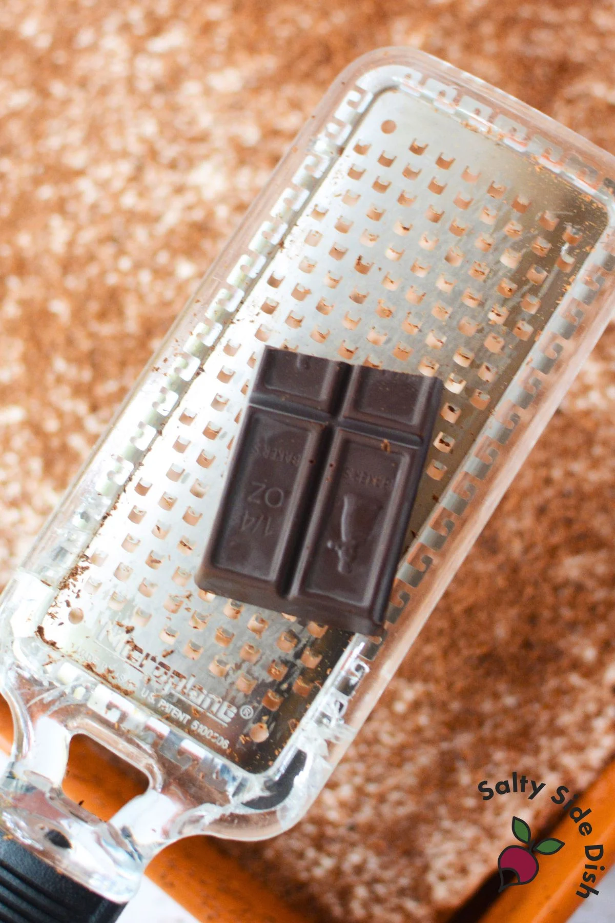 Unsweetened chocolate being grated with a microplane to top mascarpone poke cake.