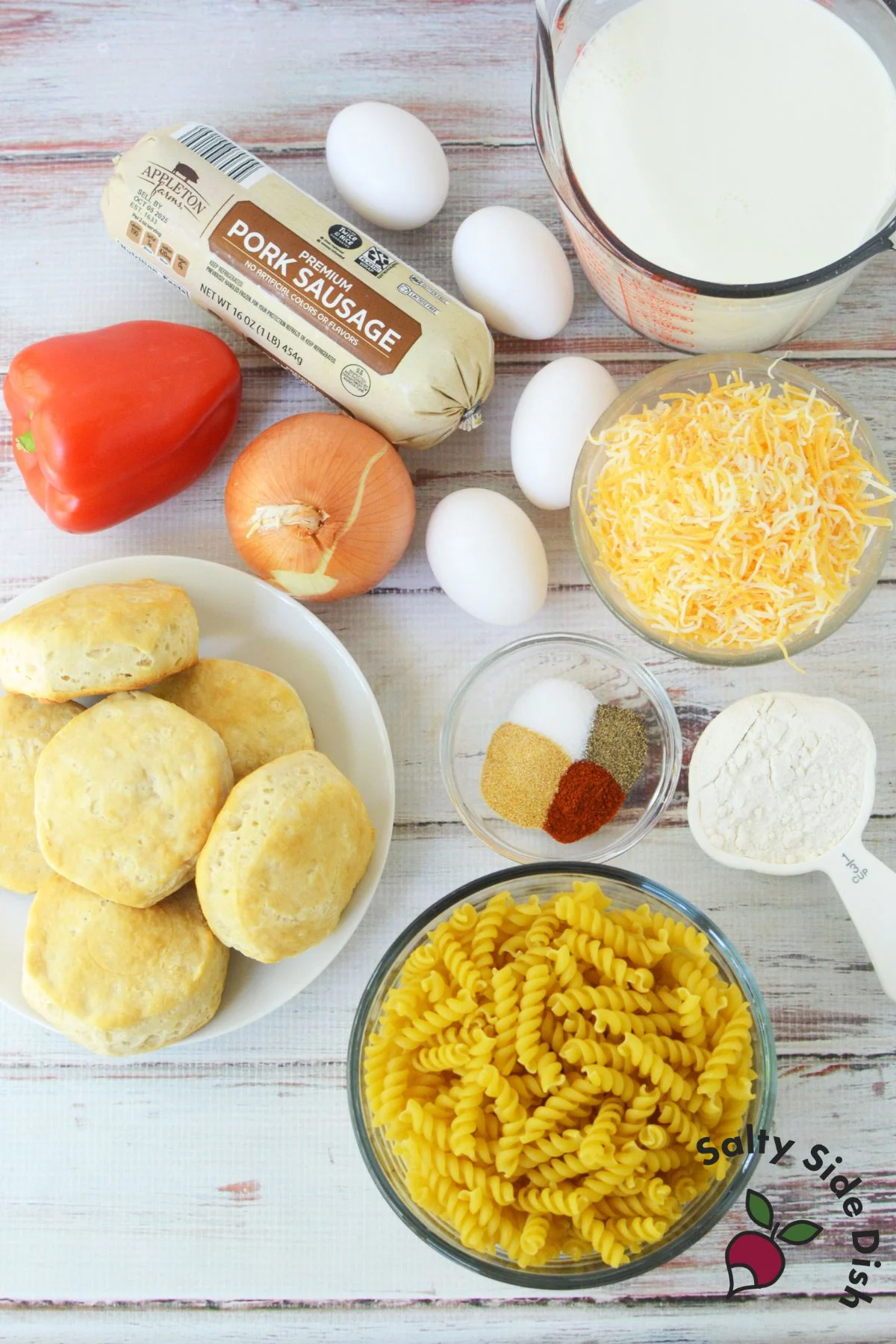 ingredients for sausage pasta bake including pasta, sausage, biscuits, eggs, cheese, onion, red pepper, and spices