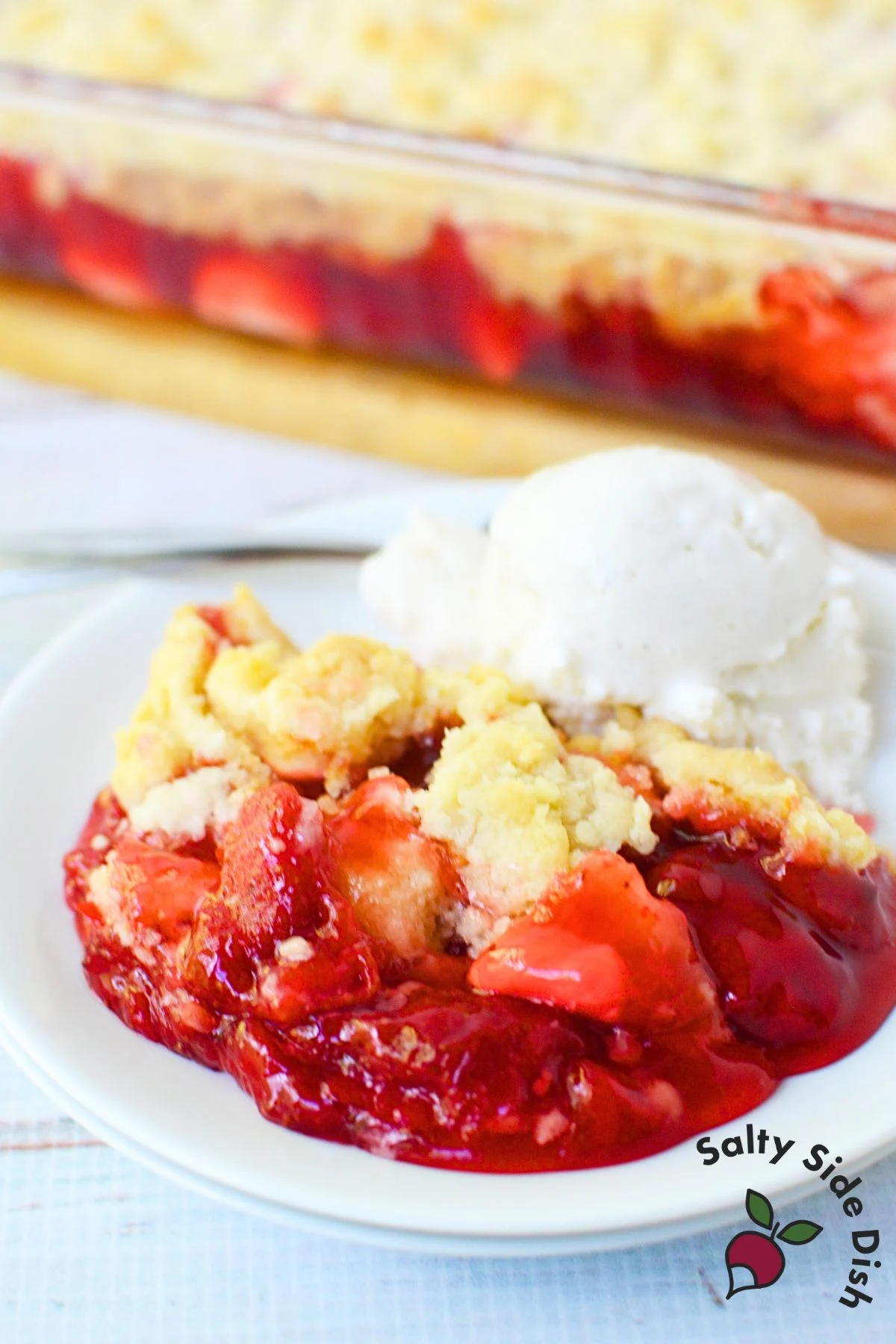 Plate of strawberry cheesecake dump cake topped with vanilla ice cream.