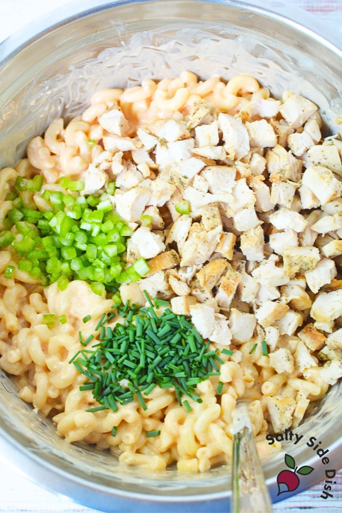 Mixing in diced chicken, celery, and chives into creamy buffalo chicken pasta salad