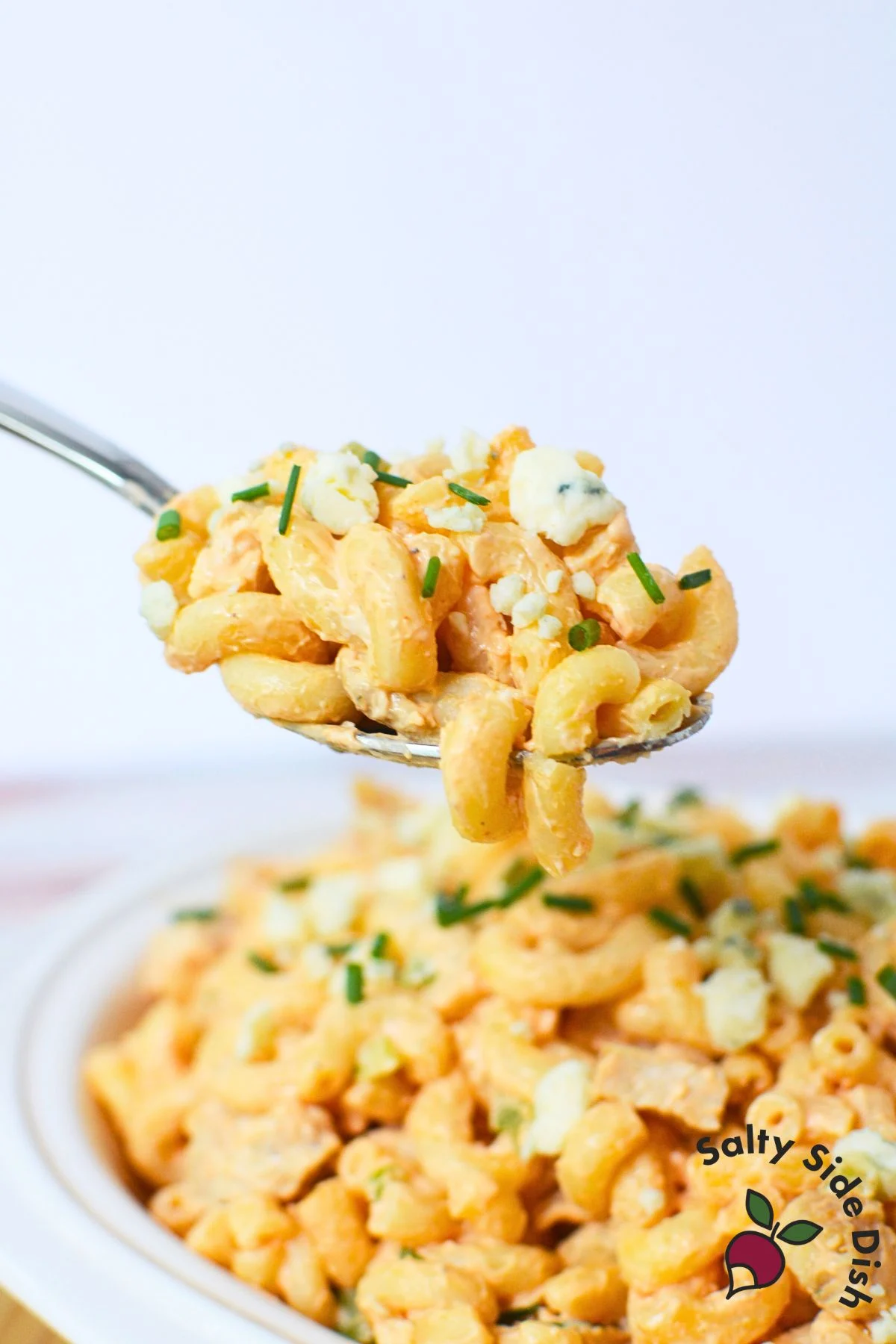 Large serving dish filled with buffalo chicken pasta salad, topped with fresh chives and cheese