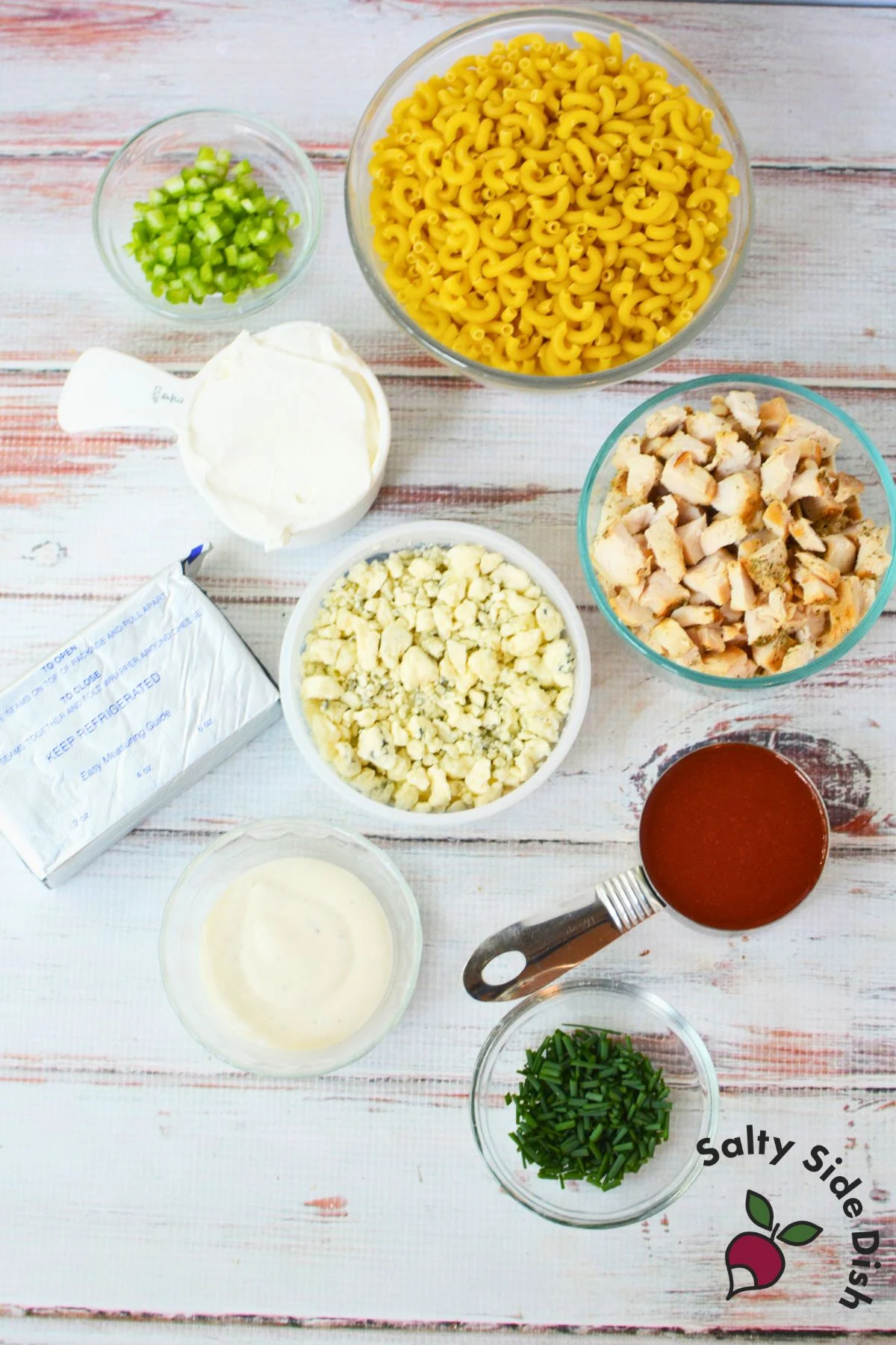 Buffalo chicken pasta salad ingredients including macaroni, chicken, hot sauce, ranch, sour cream, cream cheese, celery, and blue cheese crumbles