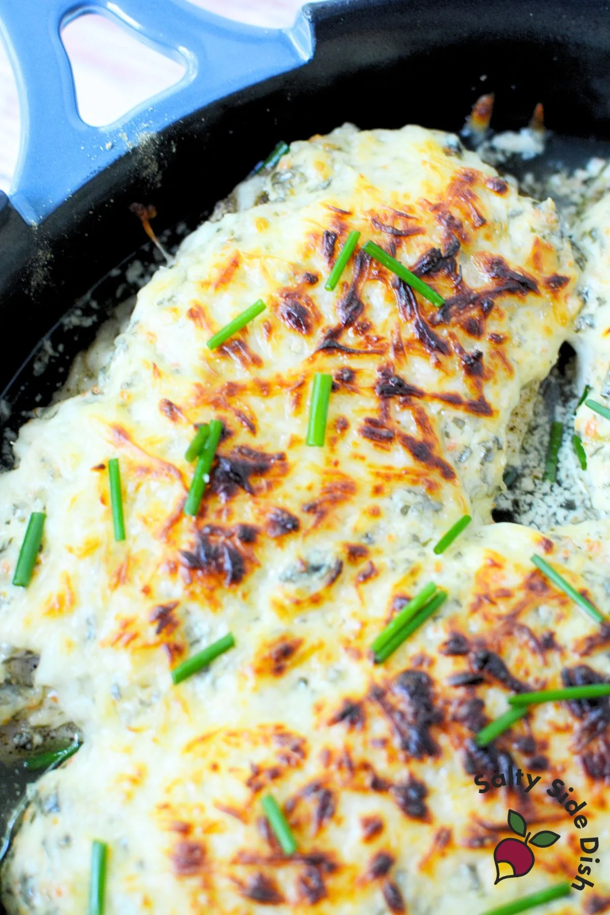 Close up of baked spinach dip chicken topped with golden mozzarella and fresh chives.