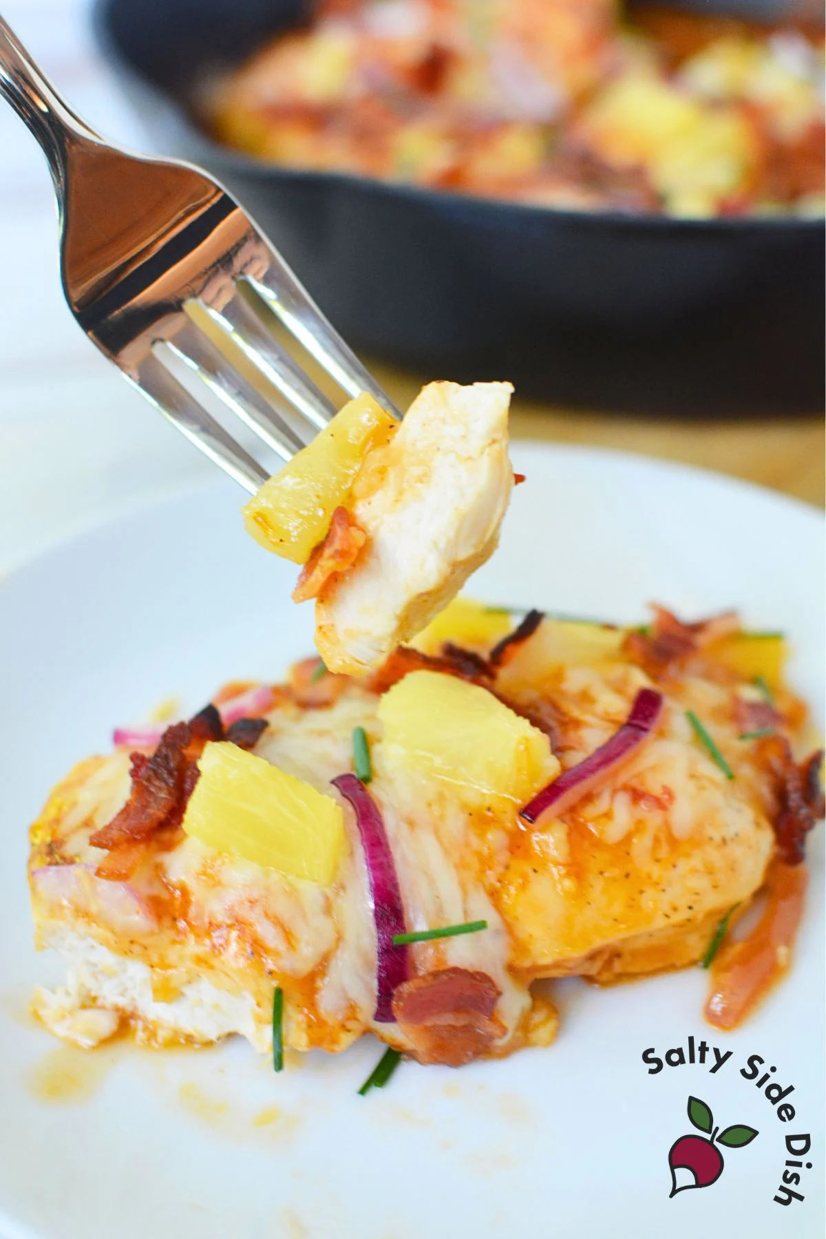 Fork holding a bite of Hawaiian chicken with pineapple, bacon, and cheese.