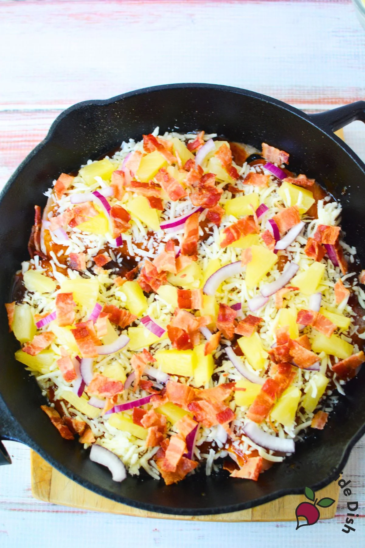 Cast iron skillet filled with baked Hawaiian chicken topped with pineapple, bacon, red onions, and cheese.
