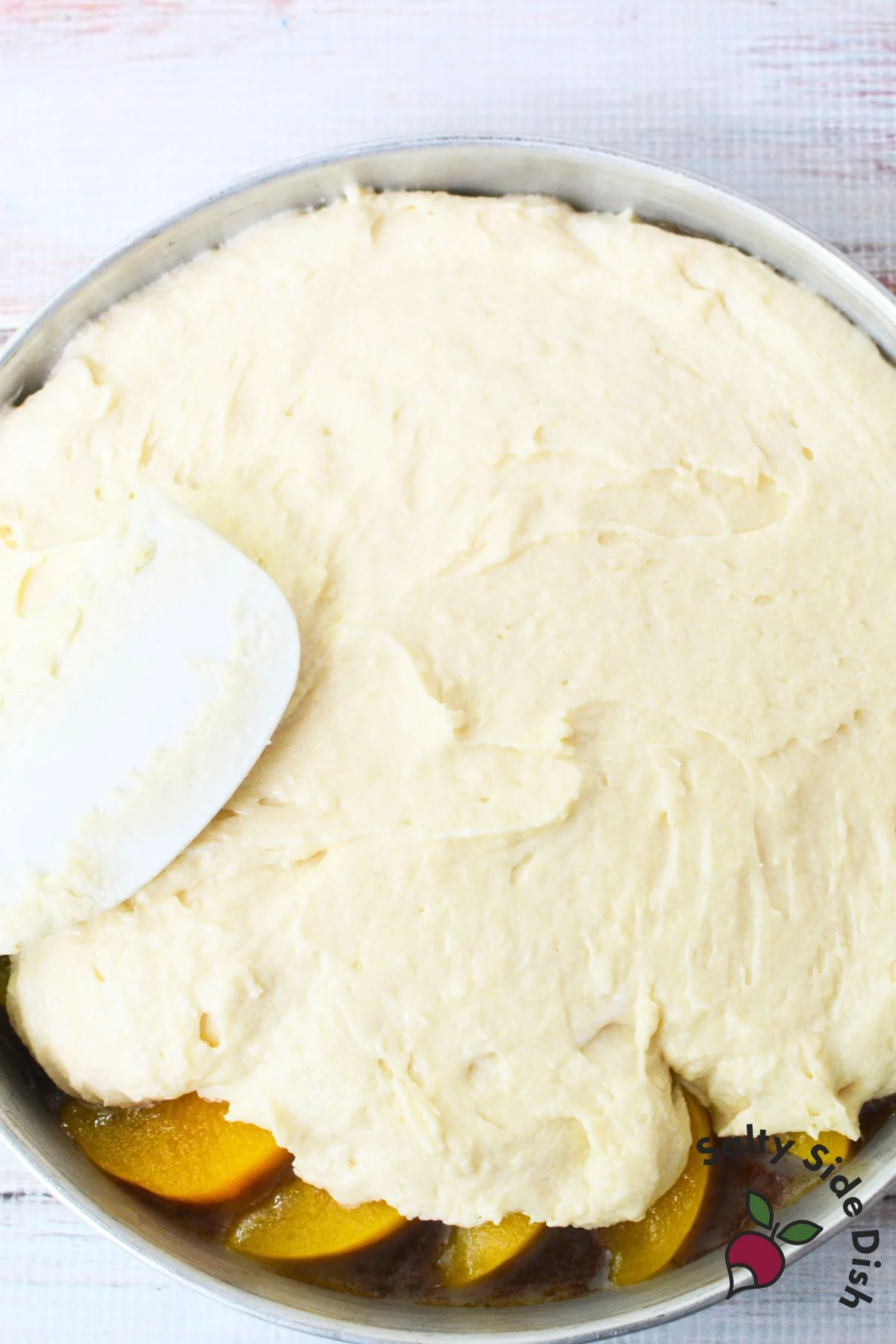 Spreading cake batter over canned peaches for upside down cake
