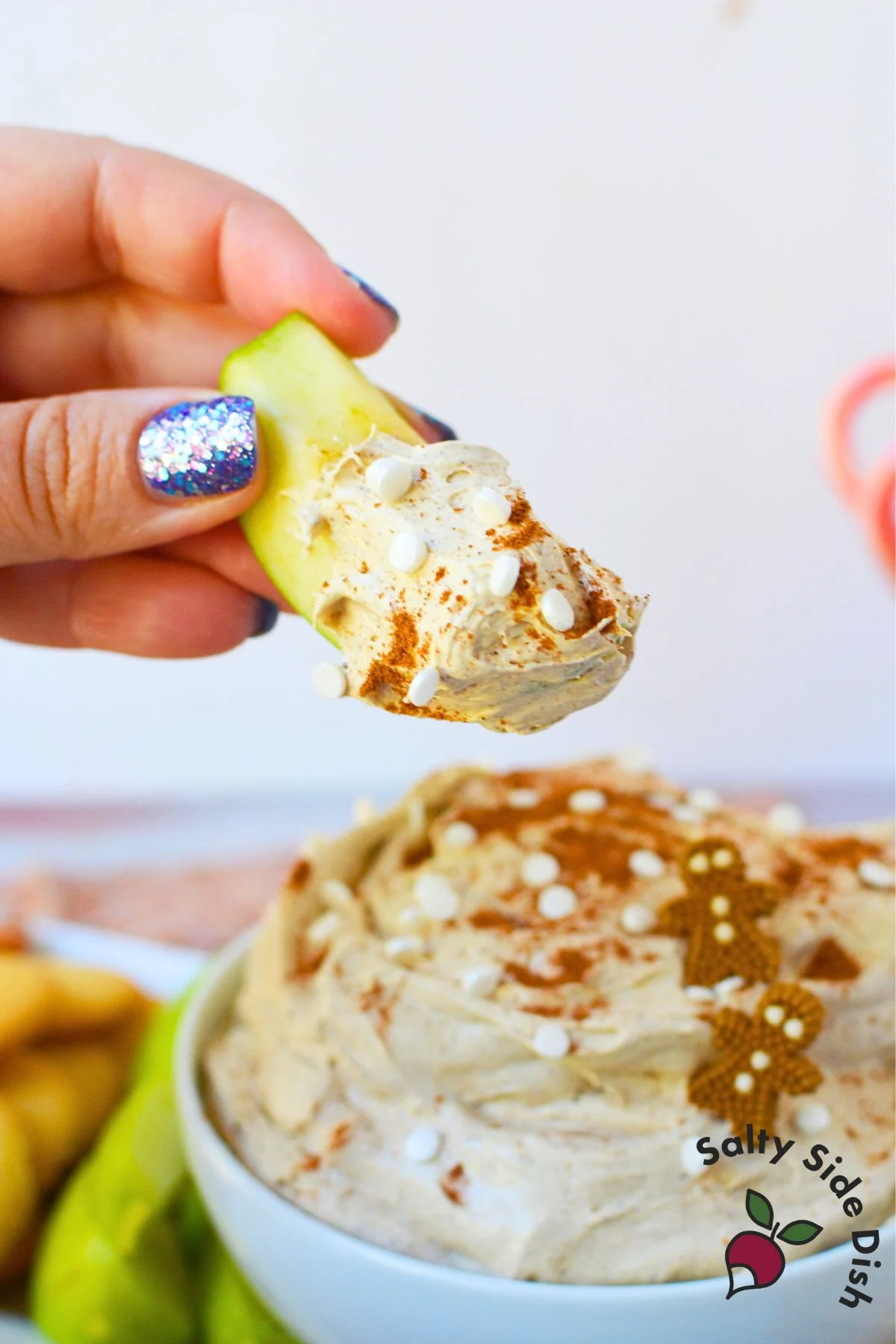 Green apple slice dipped into creamy gingerbread dip topped with cinnamon and white sprinkles.