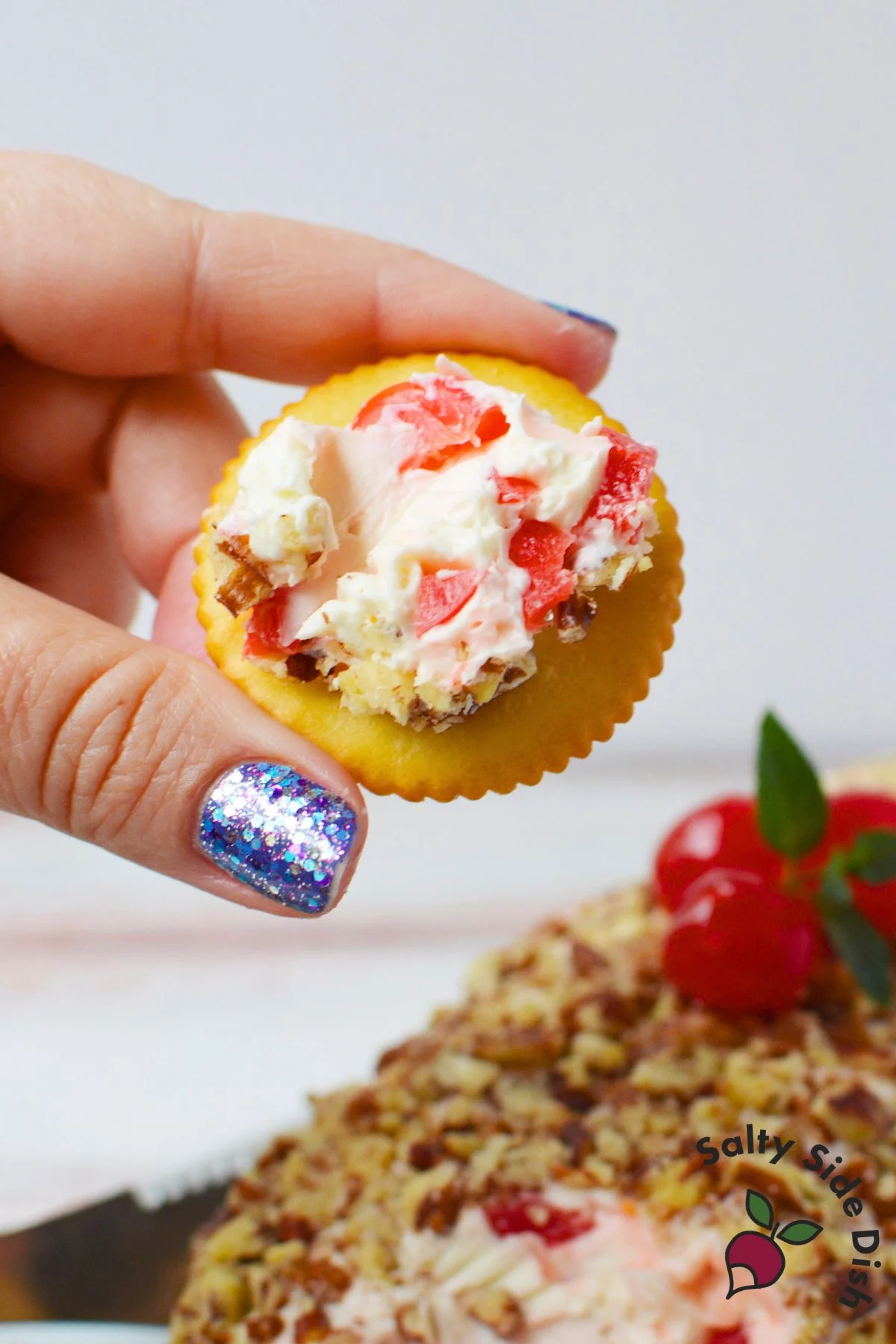 Bite of cherry cream cheese log on a cracker with maraschino cherry pieces and pecans