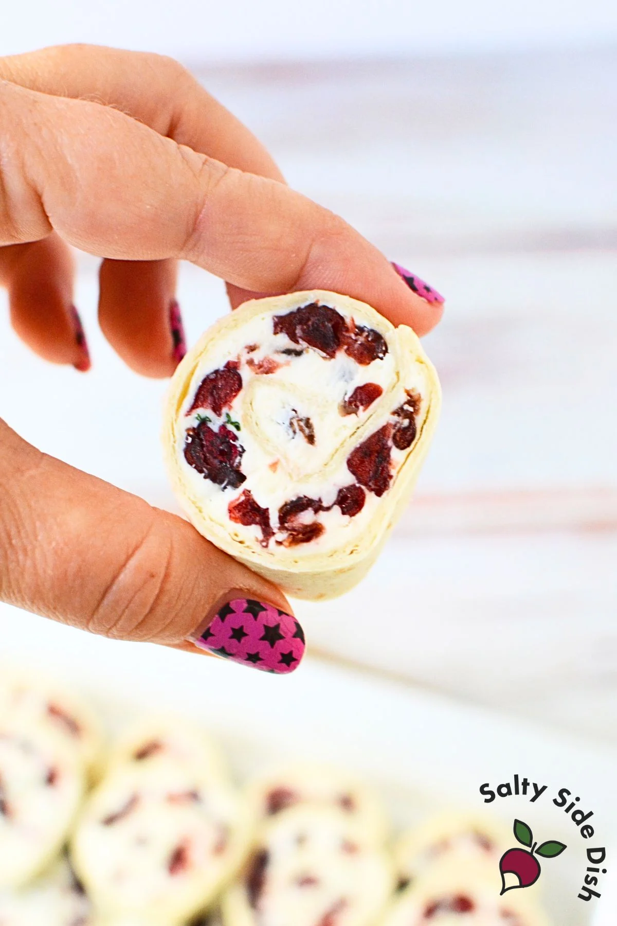 Hand holding one cranberry cream cheese pinwheel with visible cranberries and chives.