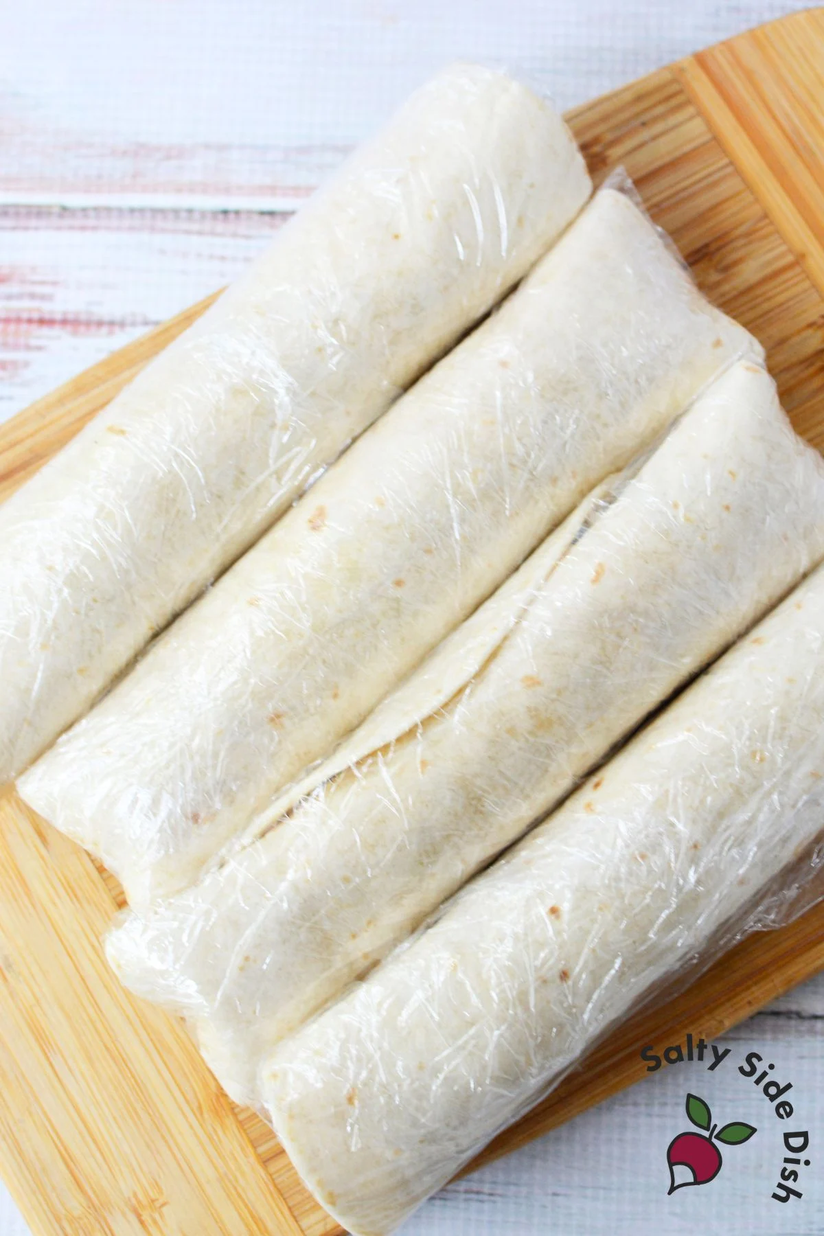 Cranberry pinwheel tortillas wrapped in plastic wrap and ready to chill in the refrigerator.