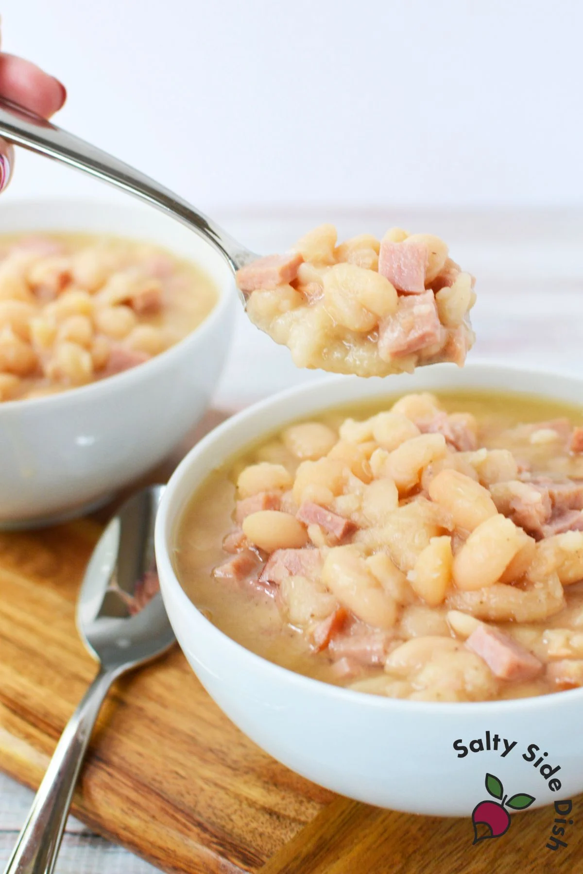Two bowls of crockpot ham and beans served with spoons
