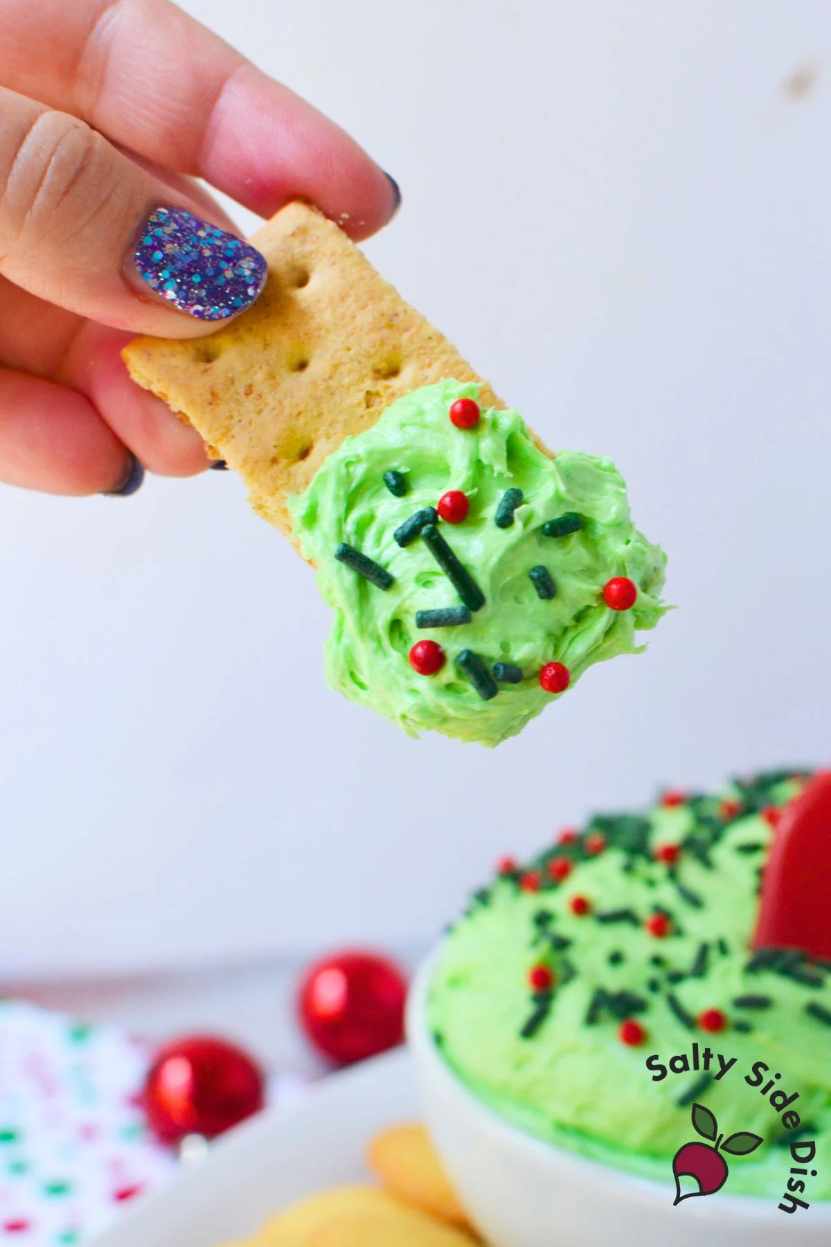 Graham cracker dipped into Whoville Christmas dip with festive red and green sprinkles