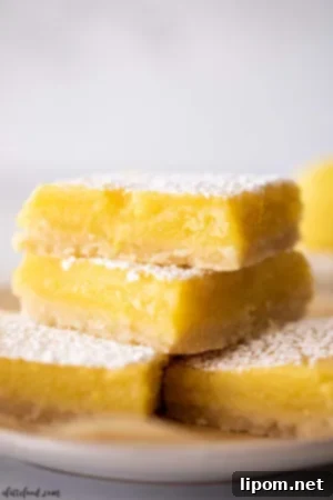 Luscious Caramel Apple Crumble Bars 5 Shortbread-crusted lemon bars stacked on a white plate, highlighting their sweet and tangy lemon custard filling topped with powdered sugar.