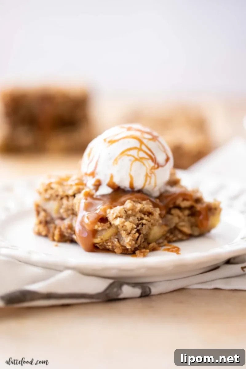Perfectly Served Caramel Apple Crumb Bar with Ice Cream Crumb-topped apple bar on a white plate with a scoop of vanilla ice cream and extra caramel sauce, emphasizing the brown sugar streusel and crisp-like crust.