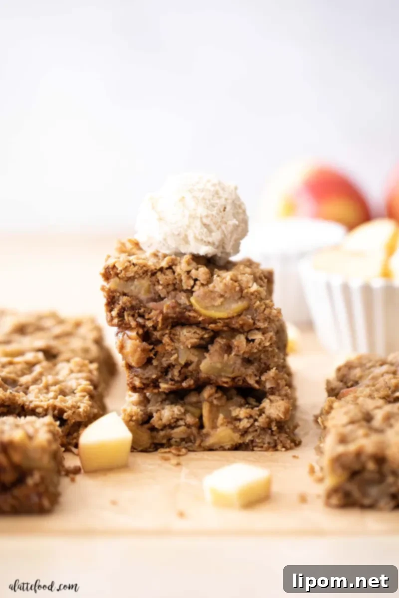 Caramel Apple Crumb Bars with Ice Cream Stack of caramel apple bars with oatmeal topping on brown parchment paper, with a scoop of ice cream on top, celebrating the blend of apple pie and apple crisp in one perfect recipe.
