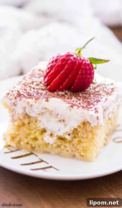 This tiramisu poke cake is soaked with a coffee cream, topped with whipped cream frosting, and each slice is served on a white plate with fresh strawberries.