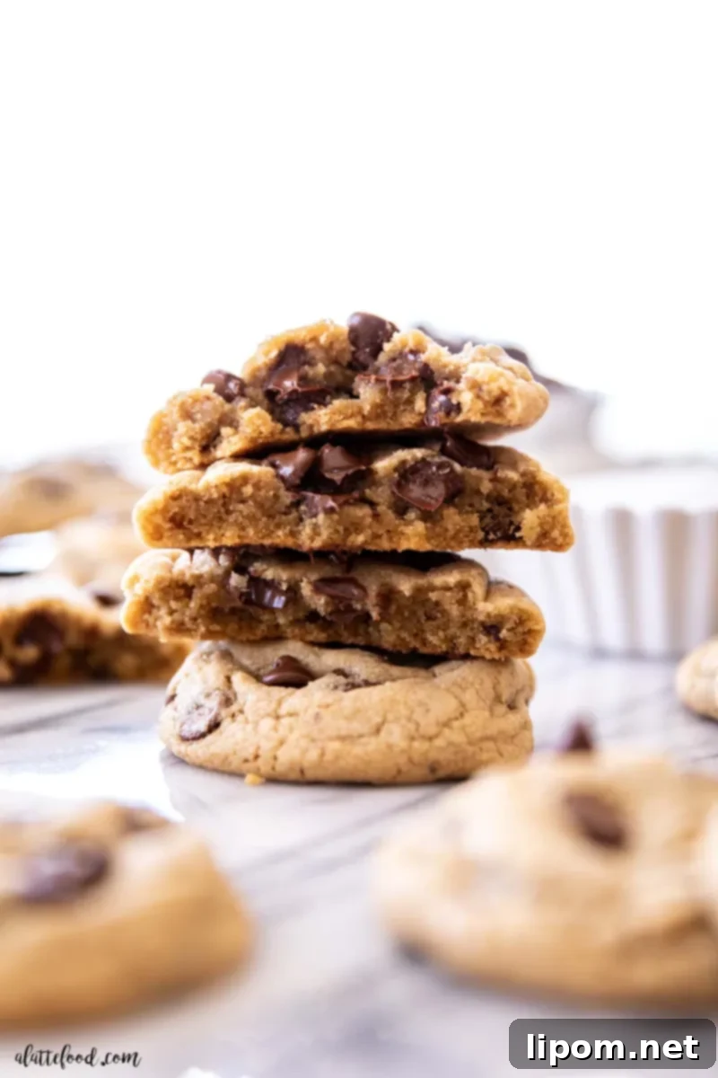 A stack of the best homemade chocolate chip cookies, richly golden brown and glistening with melted chocolate, presented invitingly on a marble board. These classic cookies are known for being soft and chewy, made with vanilla extract, espresso powder, and extra butter.