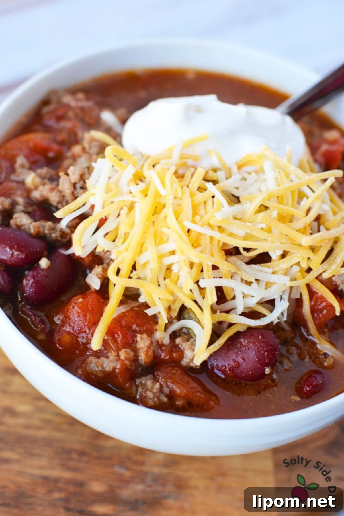 A delicious single serving of chili in a bowl, generously topped with a dollop of sour cream and a sprinkle of shredded cheese, ready to be enjoyed.