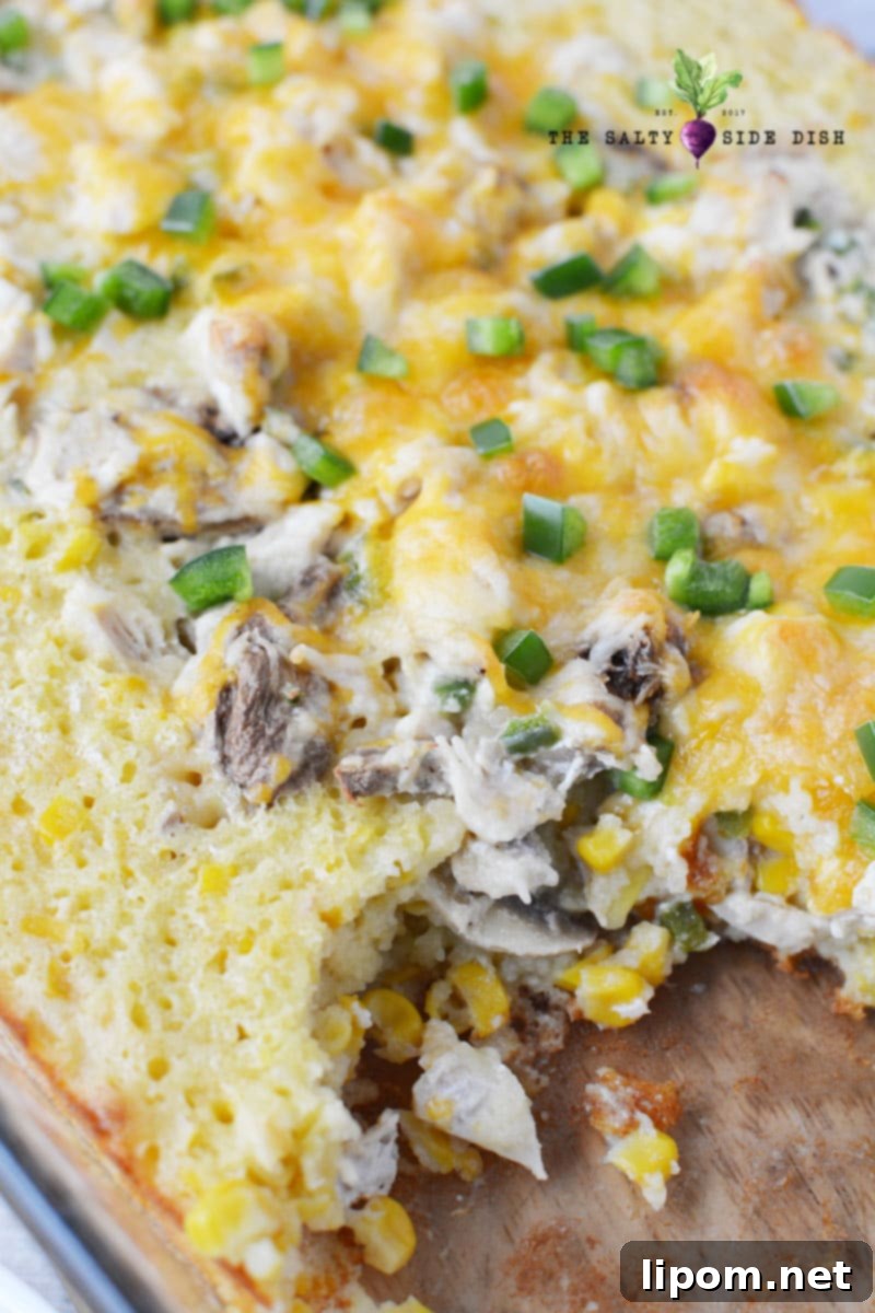 A baked Mexican cornbread casserole with a scoop removed, revealing creamy corn, chicken, and melted cheese inside.