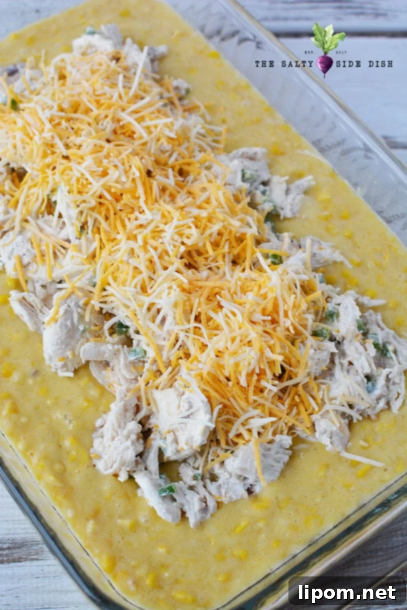 The chicken and cheese mixture spread over the cornbread base in the baking dish, leaving an edge uncovered.