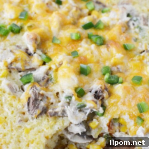A close-up shot of the Mexican Corn Casserole with Chicken, golden and bubbly, with a small portion scooped out.
