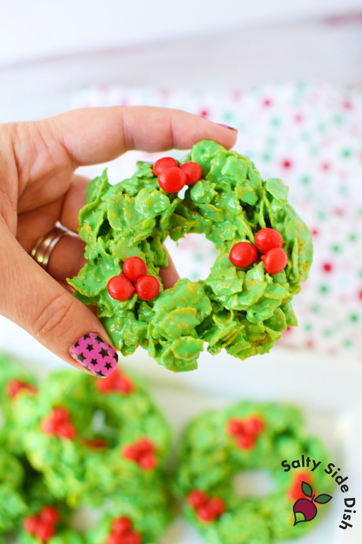 Green cornflake wreath cookies with red candies setting on a wax paper lined baking sheet.