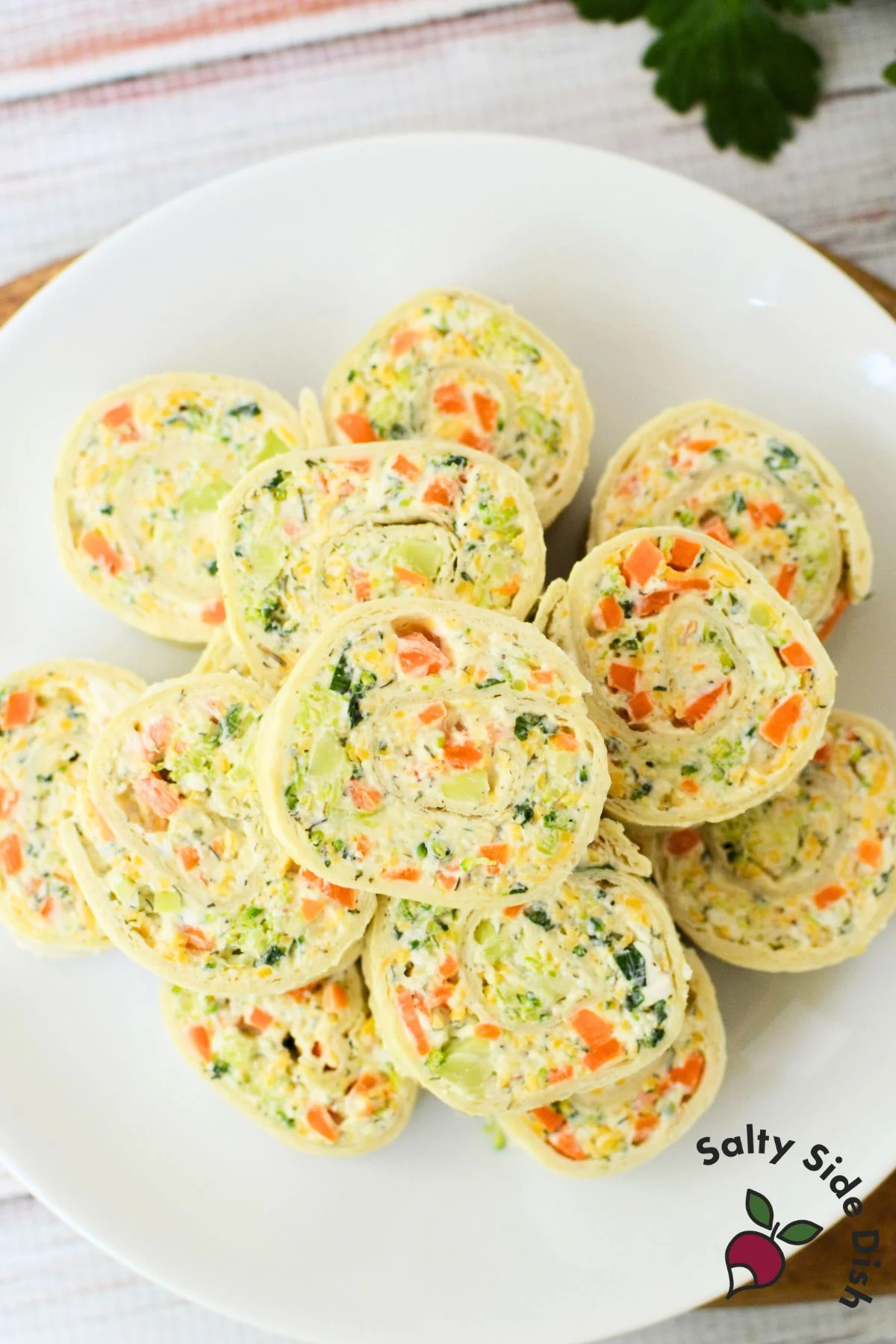 Soft tortilla being rolled up with creamy vegetable filling made from cream cheese, carrots, broccoli, and shredded cheese.