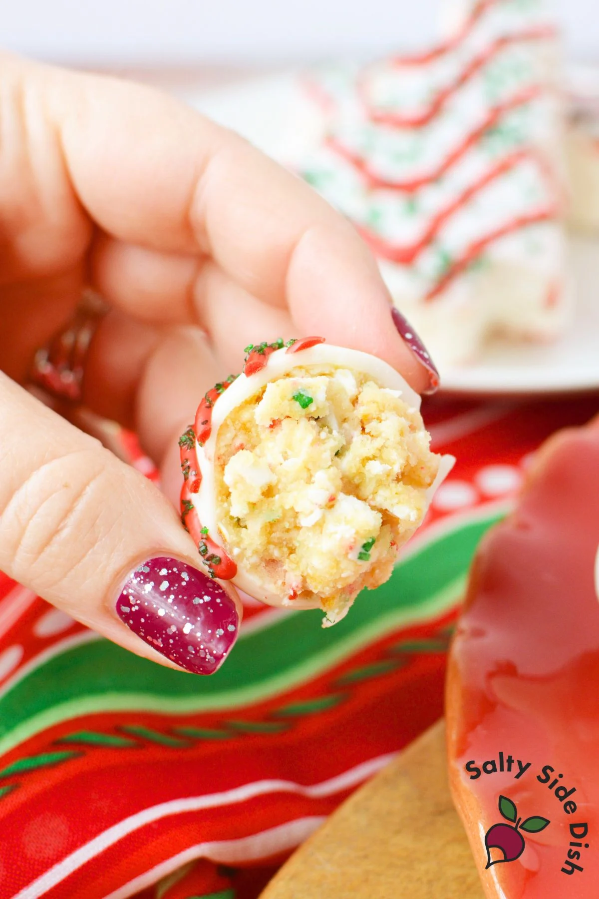 little debbie christmas tree cake ball with bite taken out, showing soft no bake cake bite center with red drizzle and green sprinkles