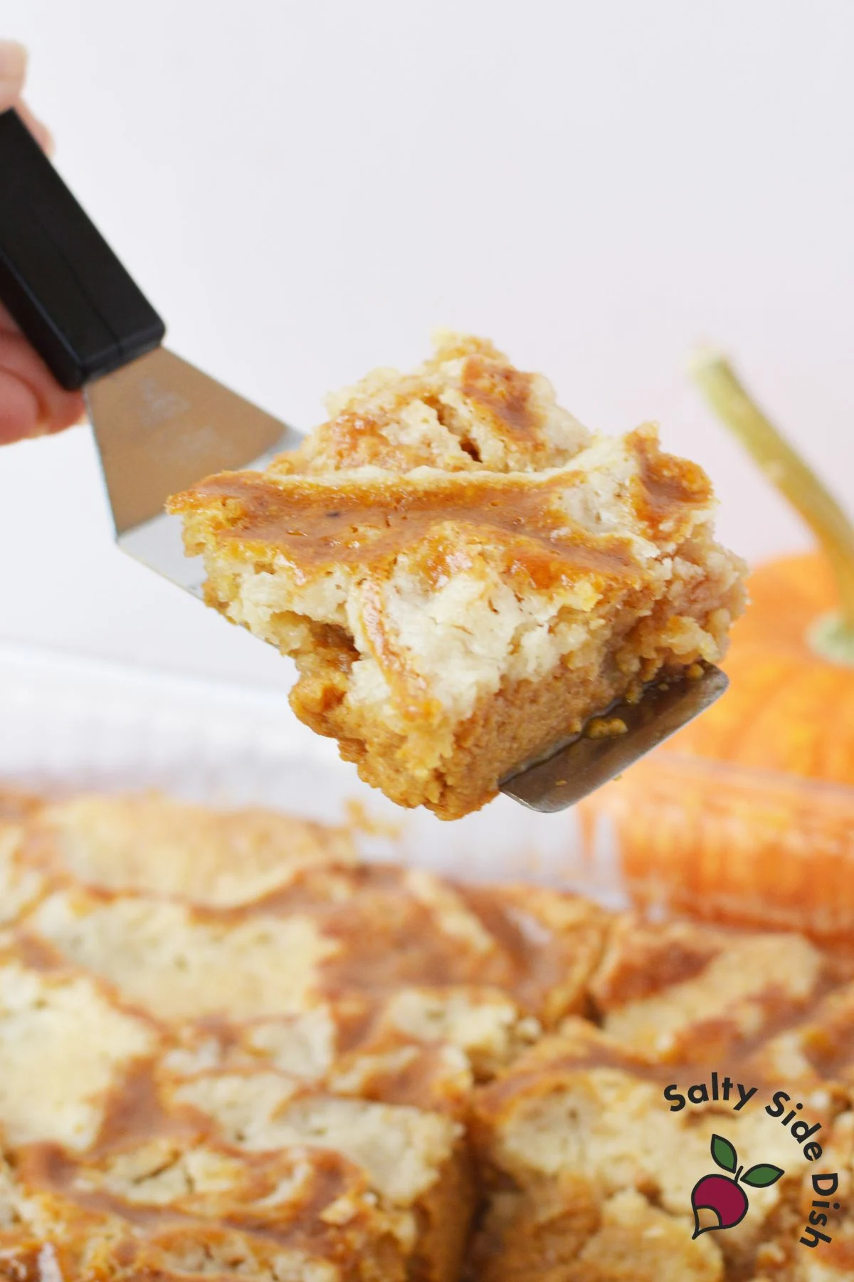 Slice of pumpkin butter cake on spatula showing gooey pumpkin layer and golden crumble topping
