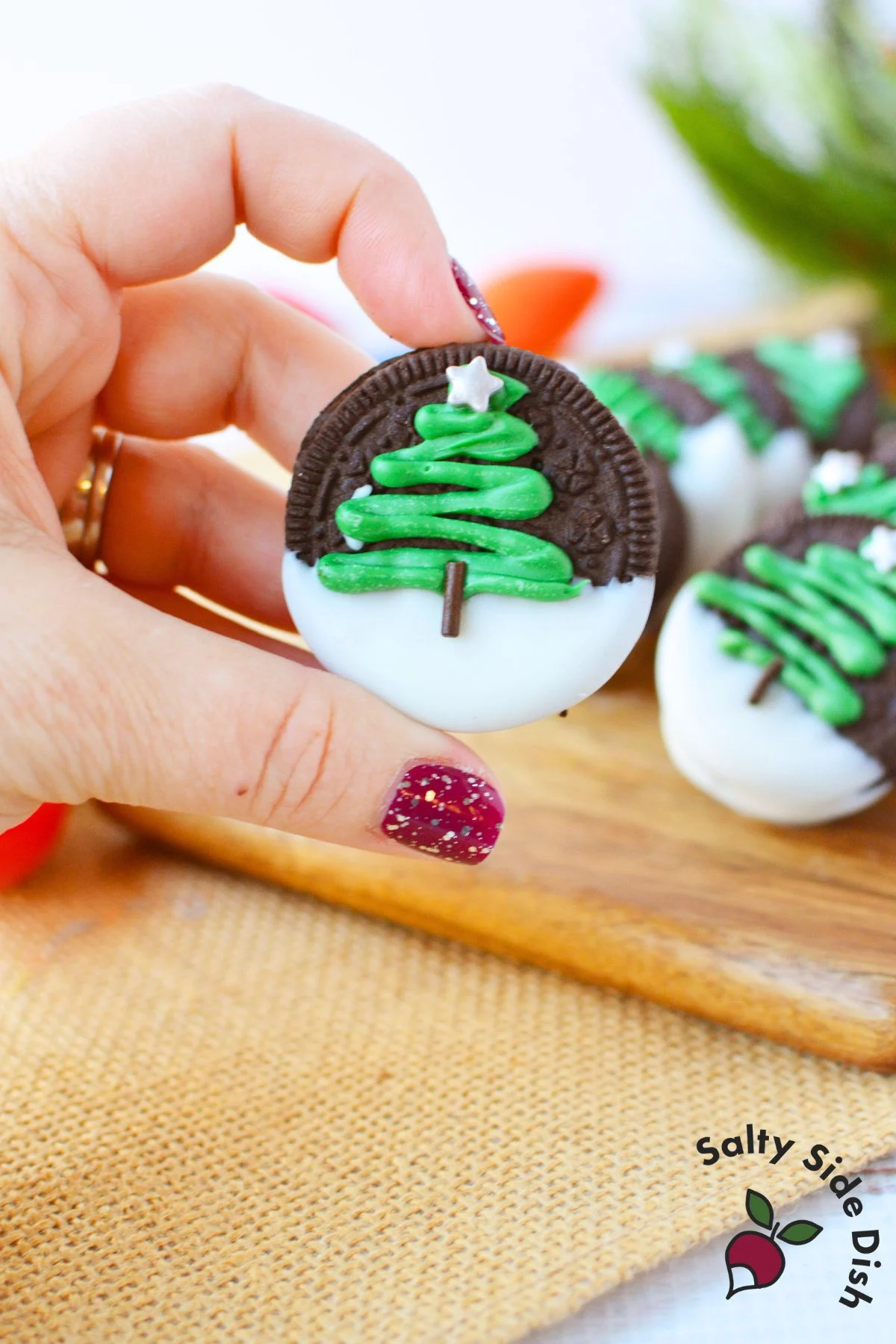 finished oreo christmas cookies with white chocolate coating and green christmas tree icing on parchment paper
