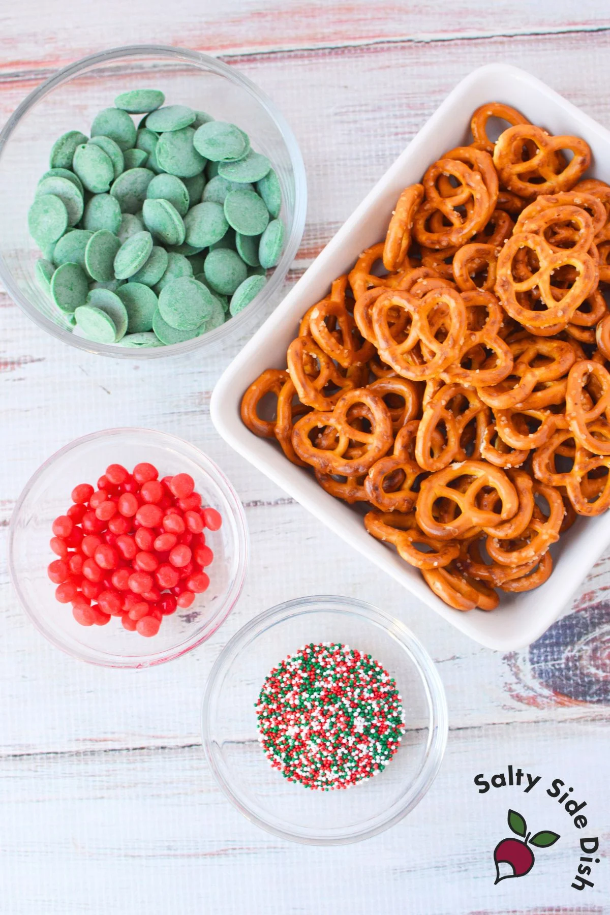 Ingredients for chocolate pretzel wreath including pretzels, green candy melts, cinnamon candies, and holiday sprinkles