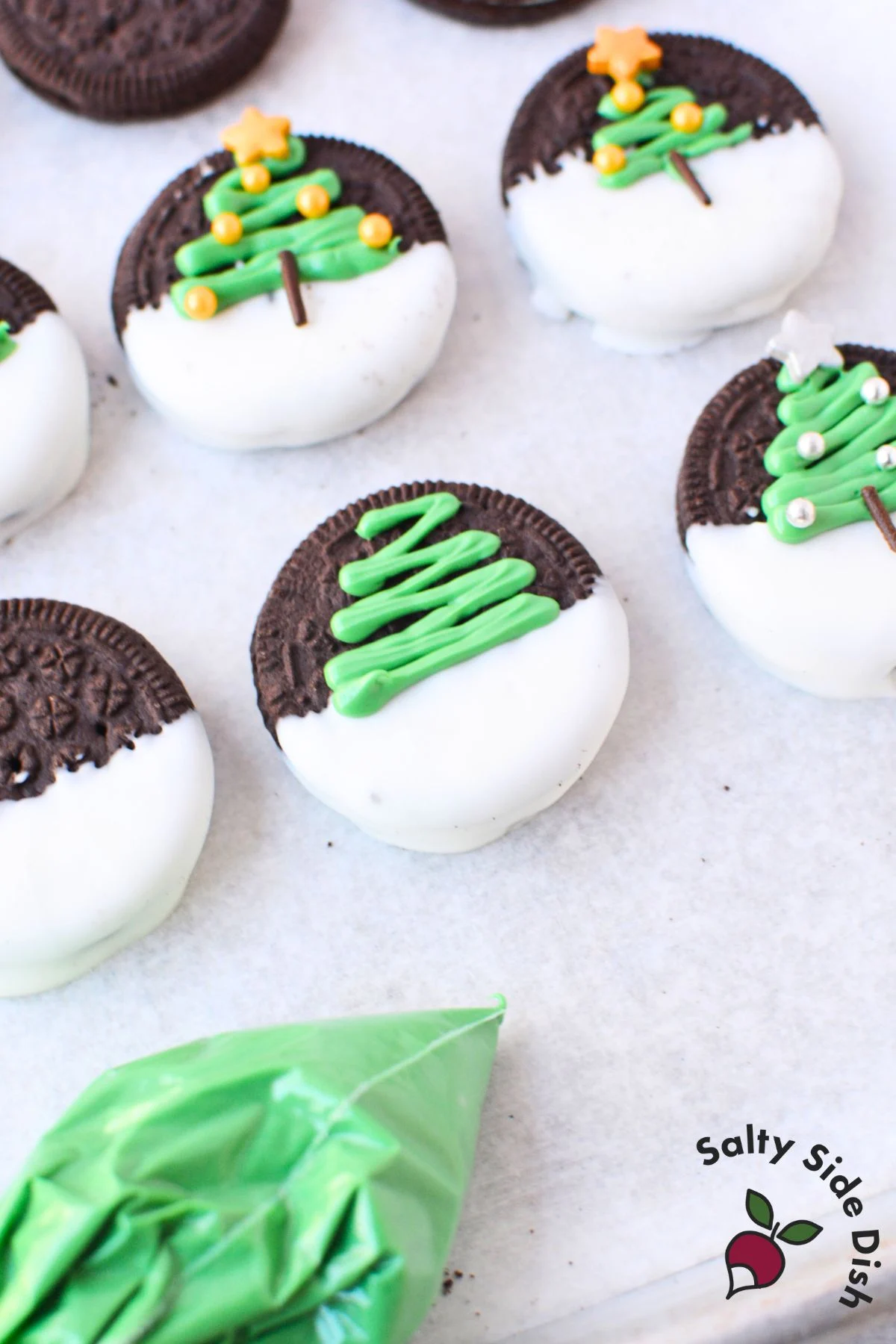 piping green candy melts onto oreos to create christmas tree designs for chocolate covered christmas oreos