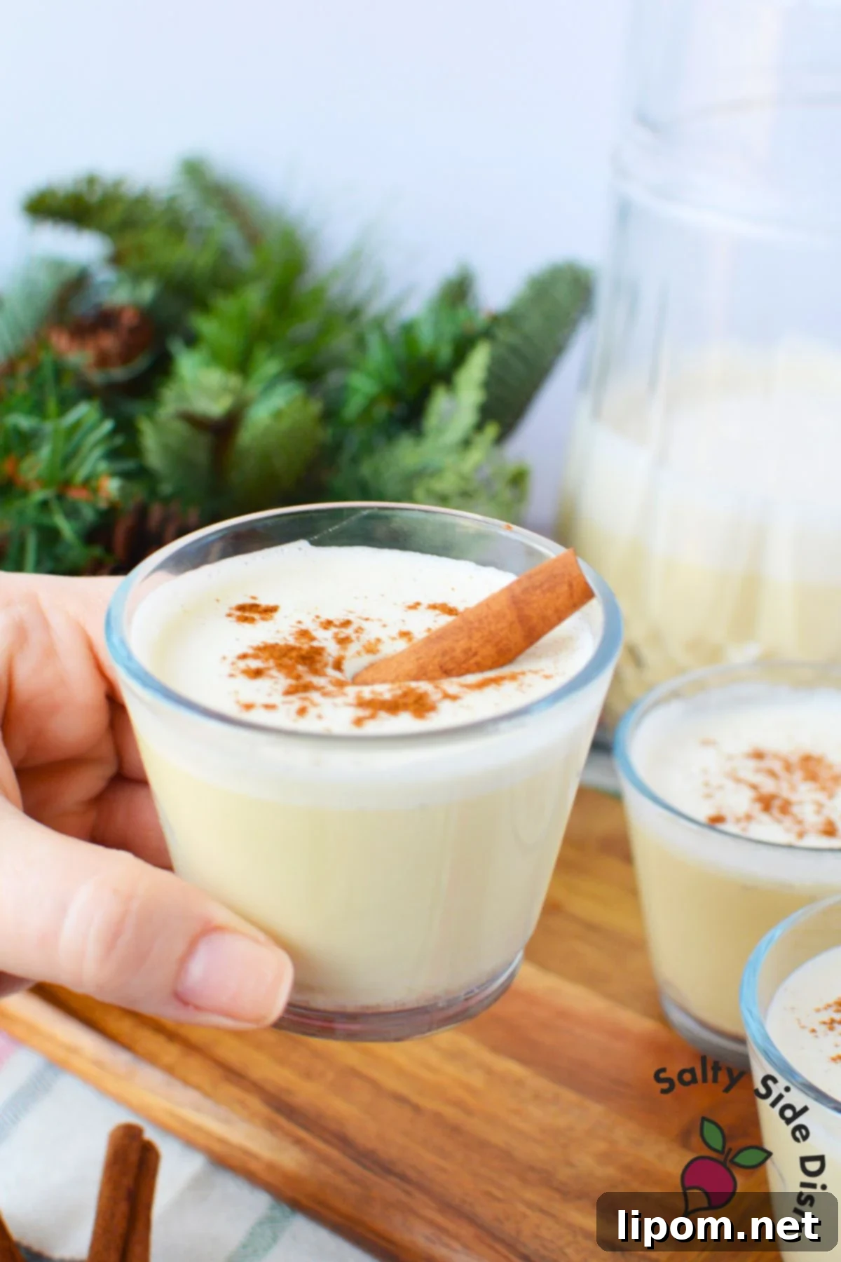 Spiked Holiday Cheer 6 A hand gently holding a glass of creamy spiked eggnog, made with pasteurized whole eggs and garnished with a sprinkle of cinnamon, showcasing its deliciousness and inviting aroma.