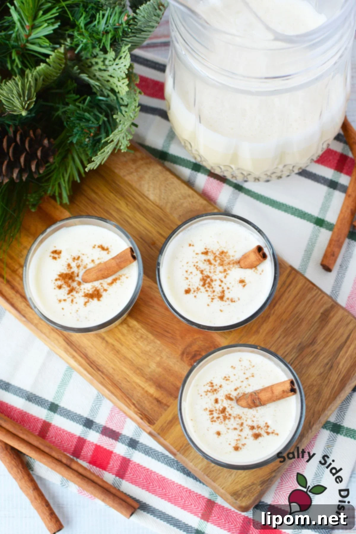 Spiked Holiday Cheer 7 Small glasses filled with creamy spiked eggnog, delicately topped with ground cinnamon, arranged on a rustic wooden serving board, creating an inviting and festive presentation.