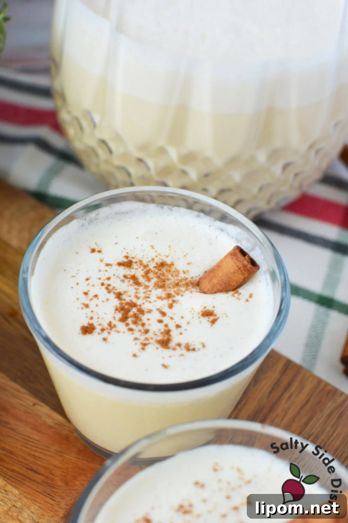 Spiked Holiday Cheer 8 A close-up shot of spiked eggnog served in a clear glass, beautifully garnished with a cinnamon stick, capturing the essence of a perfect Christmas eggnog serving.